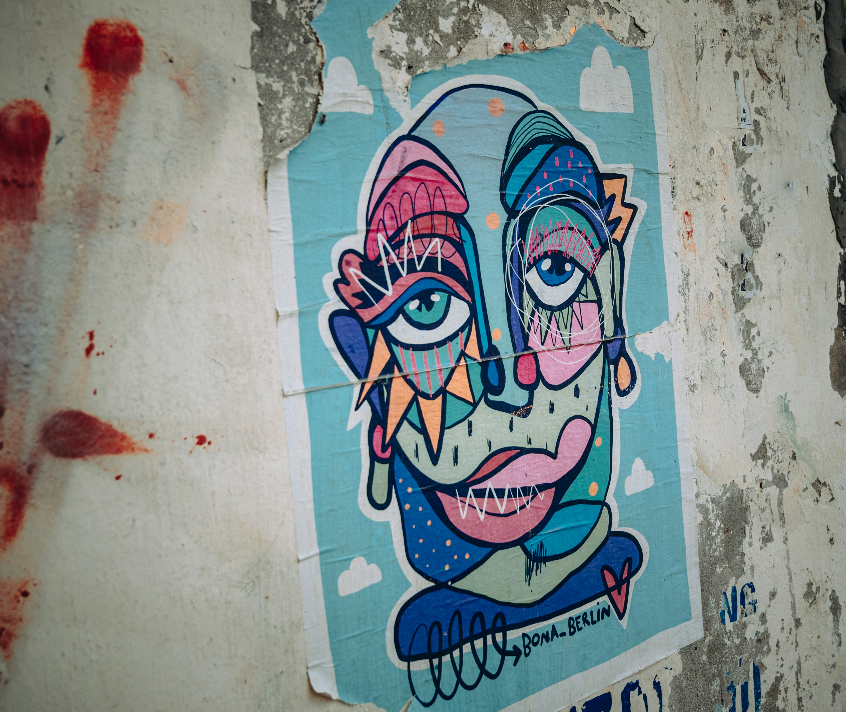 A colorful abstract face illustration on a torn poster attached to a weathered wall