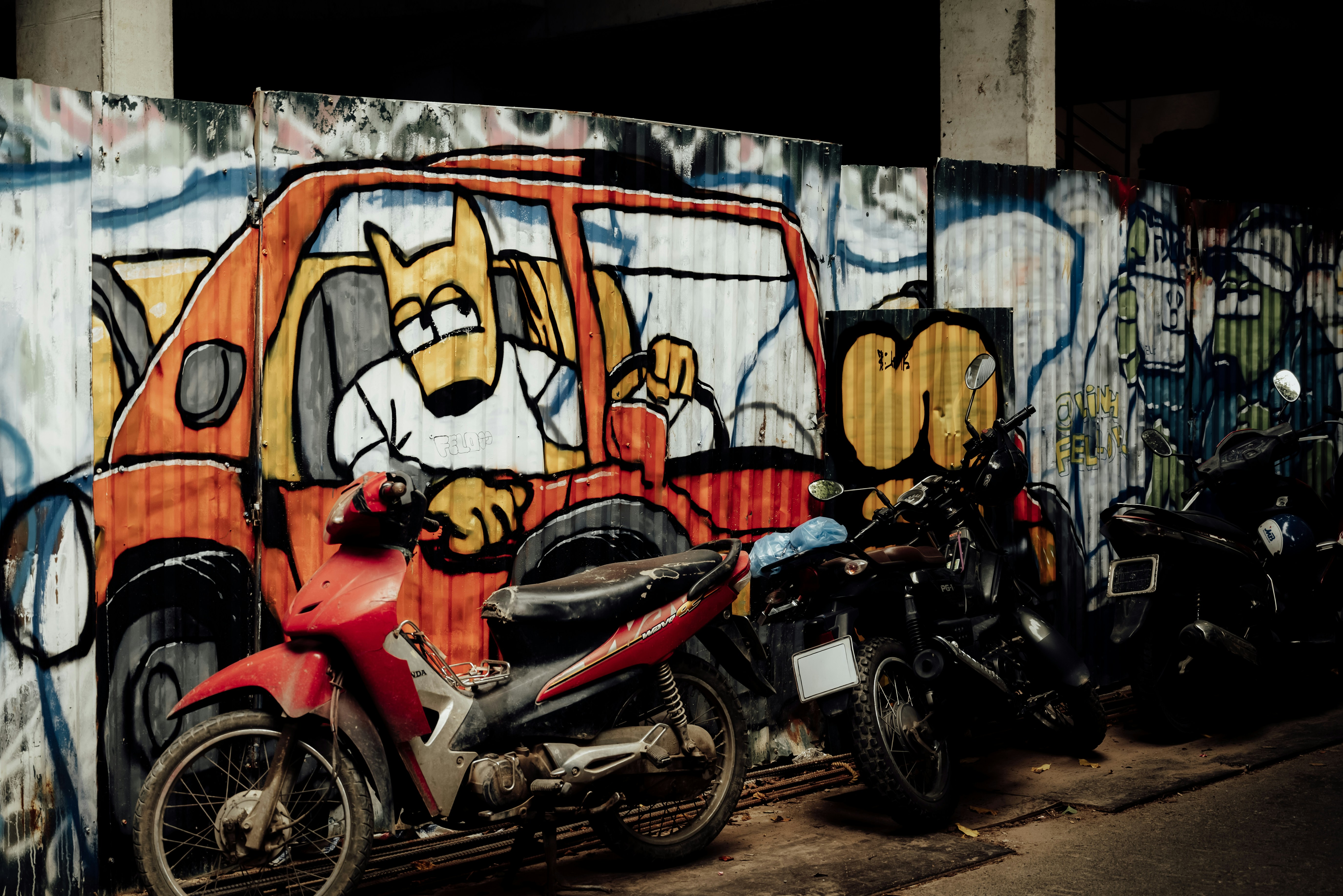 Motorbikes parked against a corrugated metal fence painted with a cartoon car mural