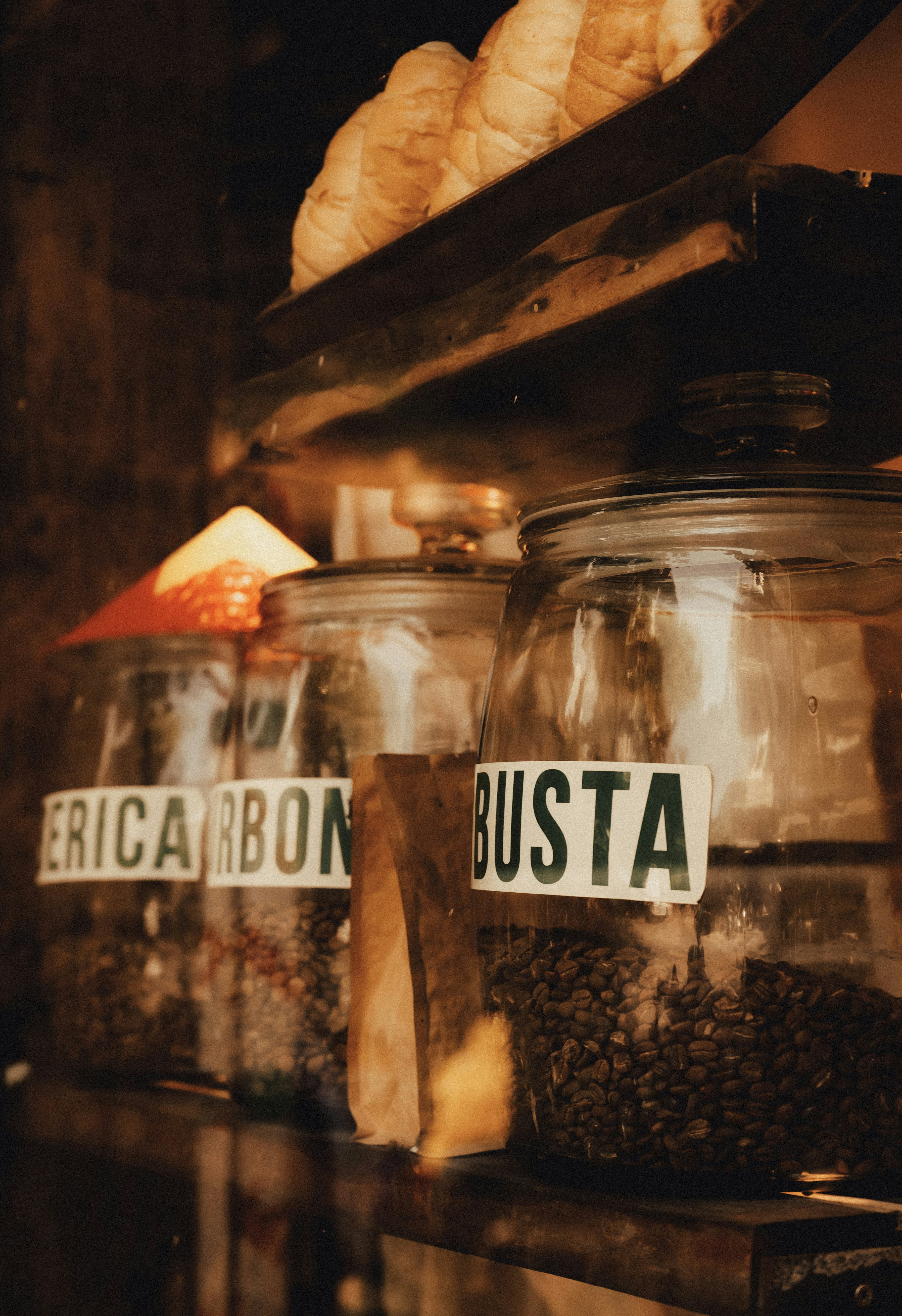 Glass jars filled with coffee beans on a wooden shelf with croissants above