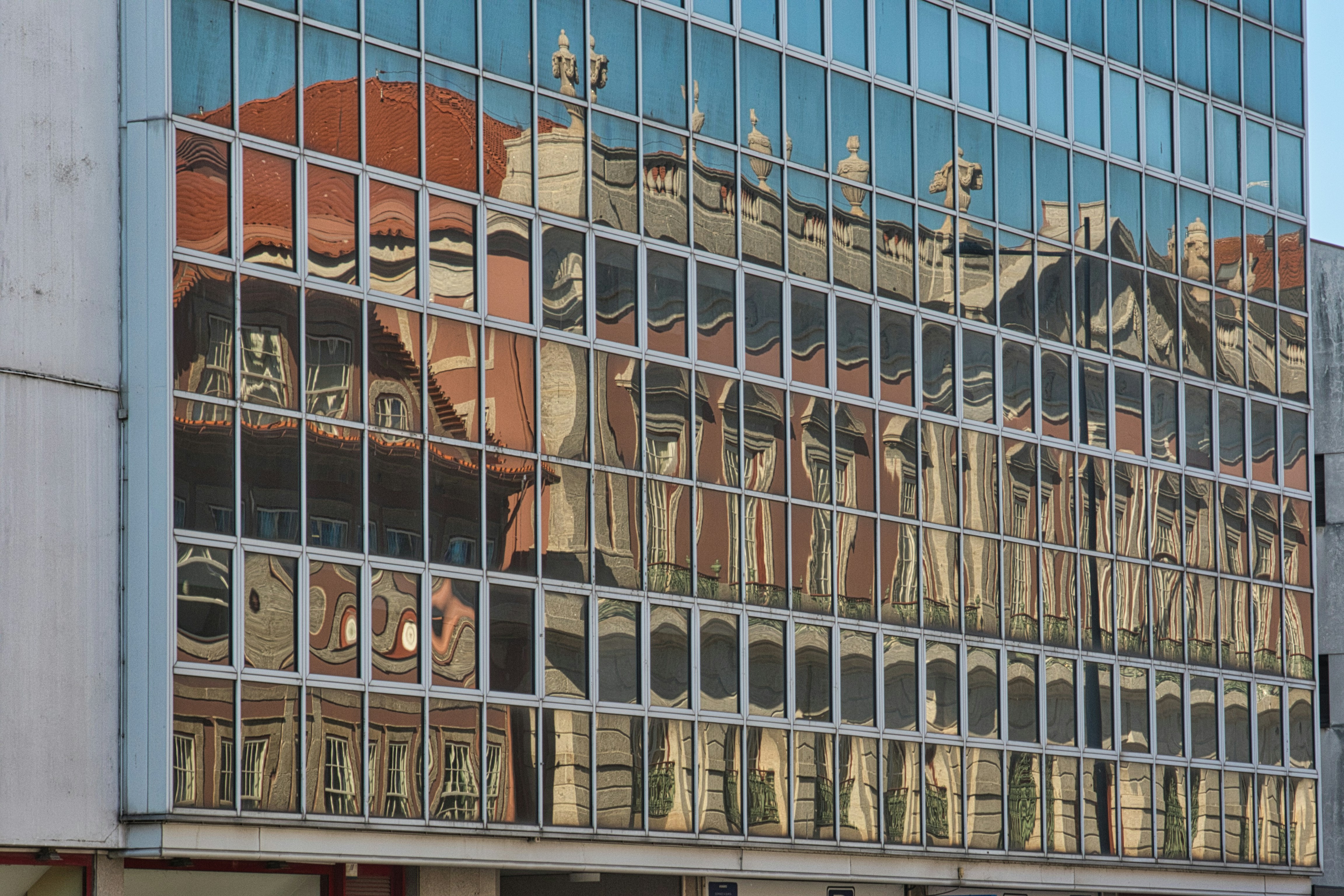 A historic red building reflected in the glass facade of a modern office building