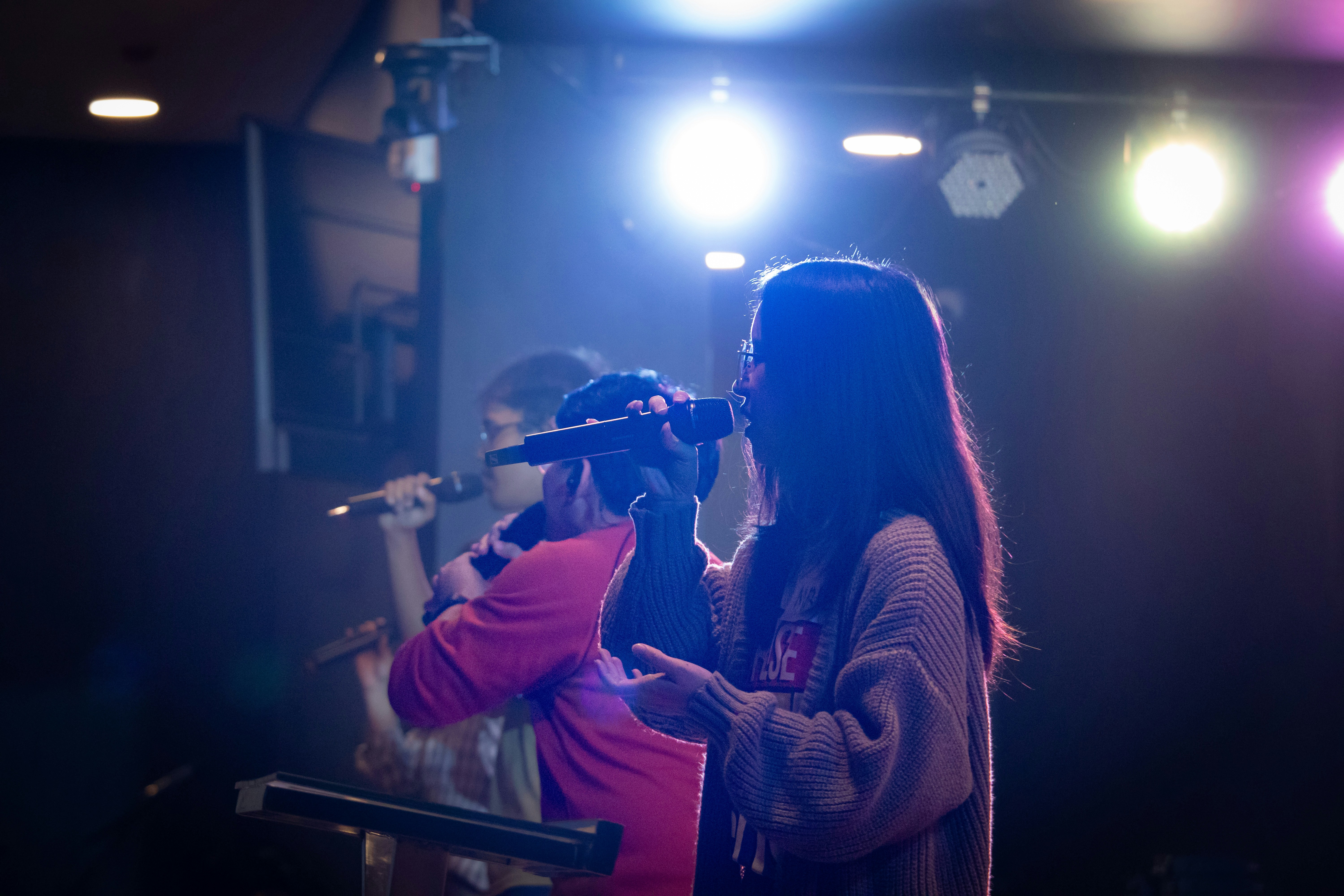 A woman singing into a microphone on a stage with colorful spotlights