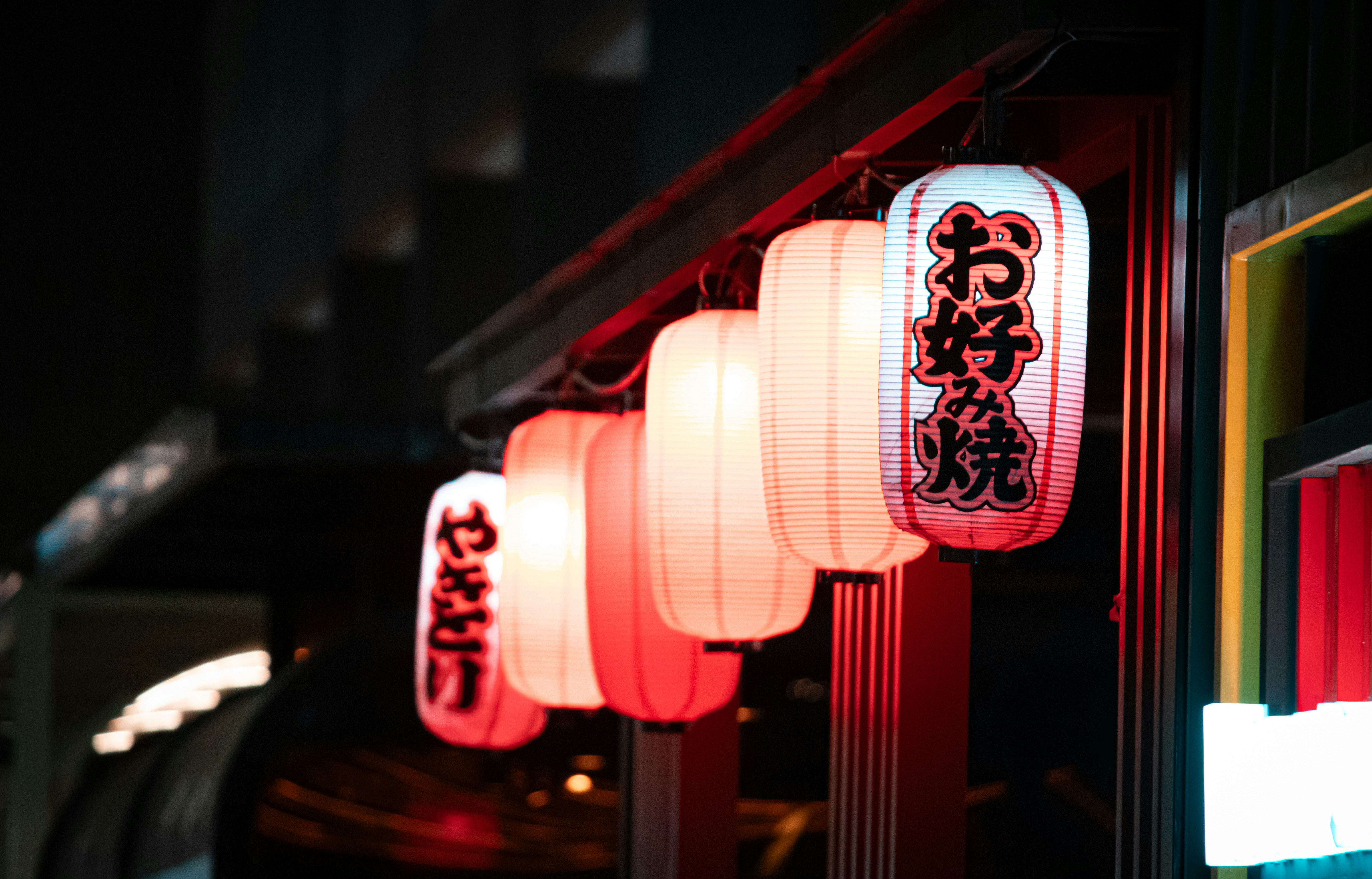 A row of glowing paper lanterns with Japanese characters hanging at night