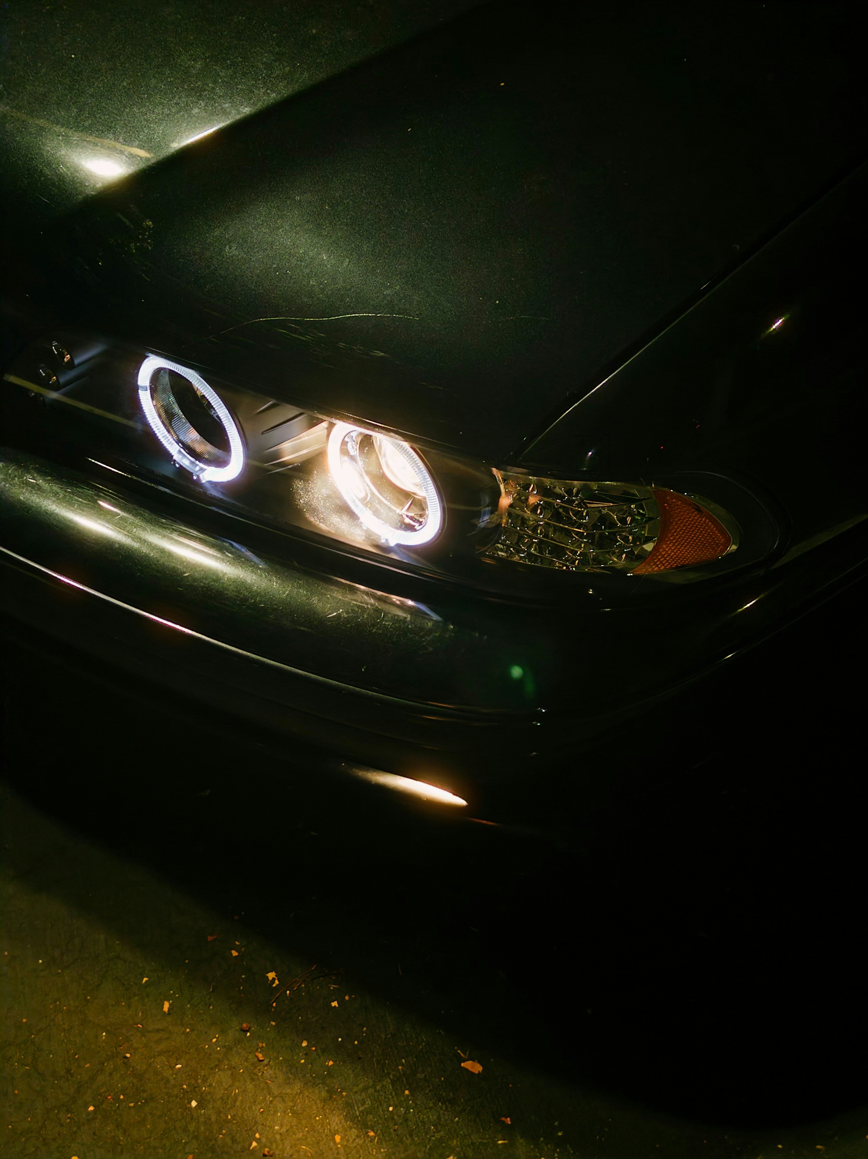 Un coche oscuro con faros circulares de halo blanco brillante por la noche