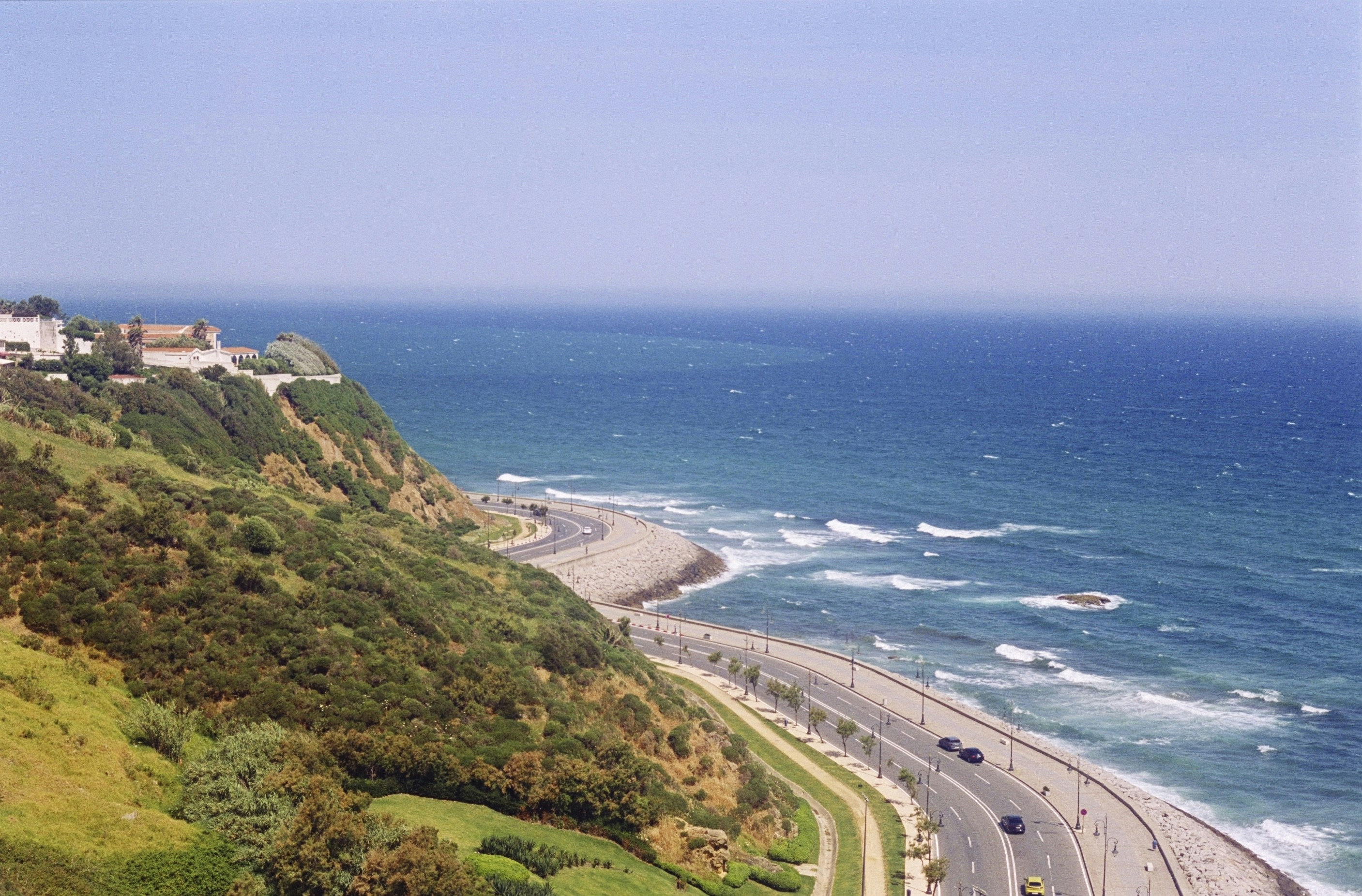 A coastal road winding along a green cliffside above the blue ocean
