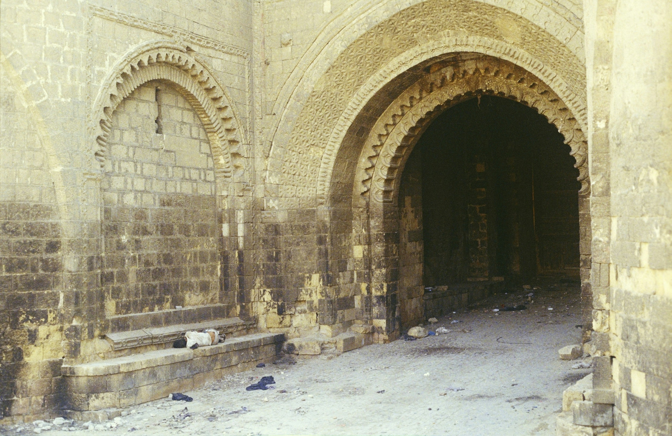 A person lying on a stone bench inside a weathered arched stone gateway