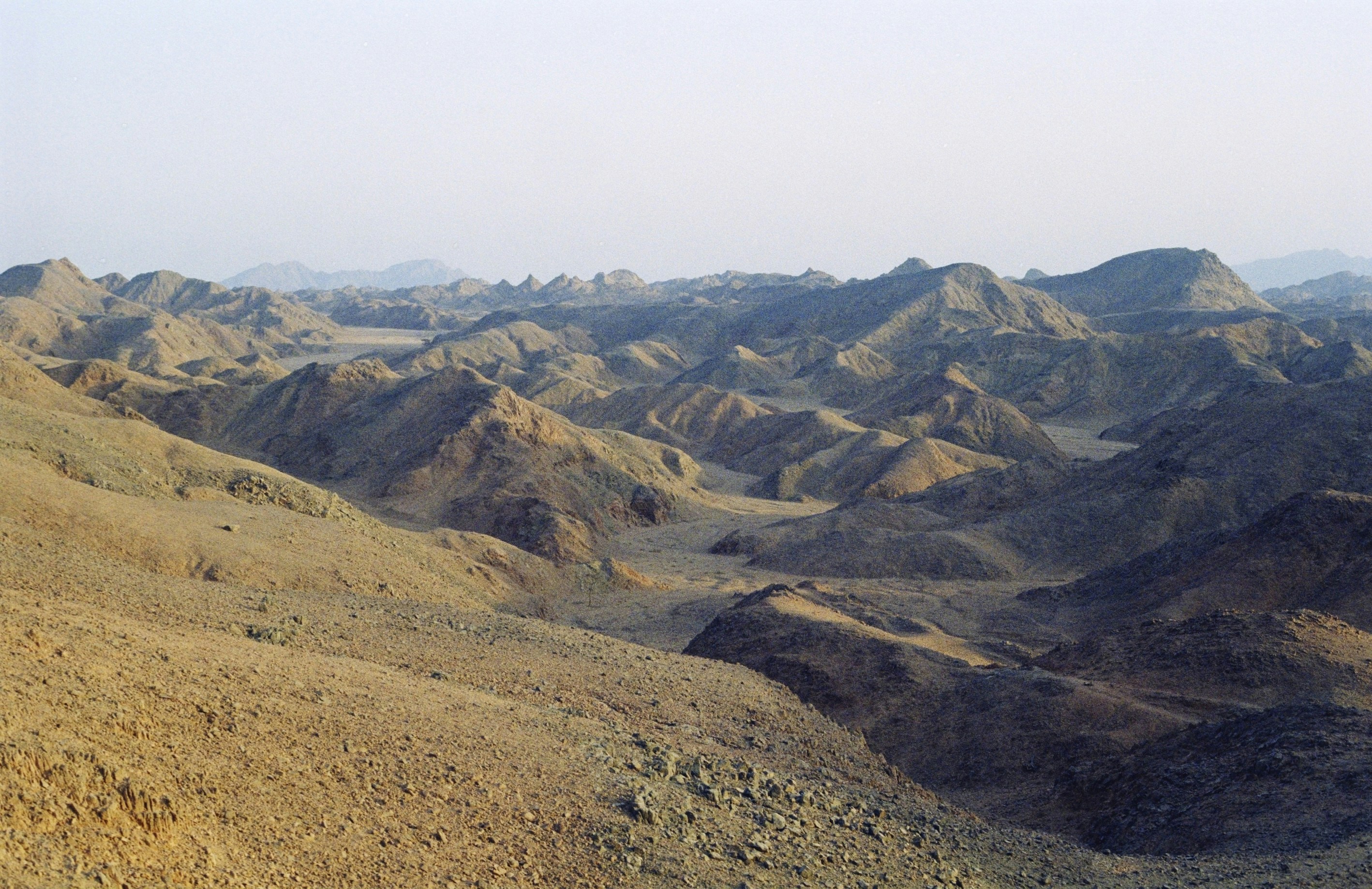 Arid brown mountains and rolling hills under a pale hazy sky