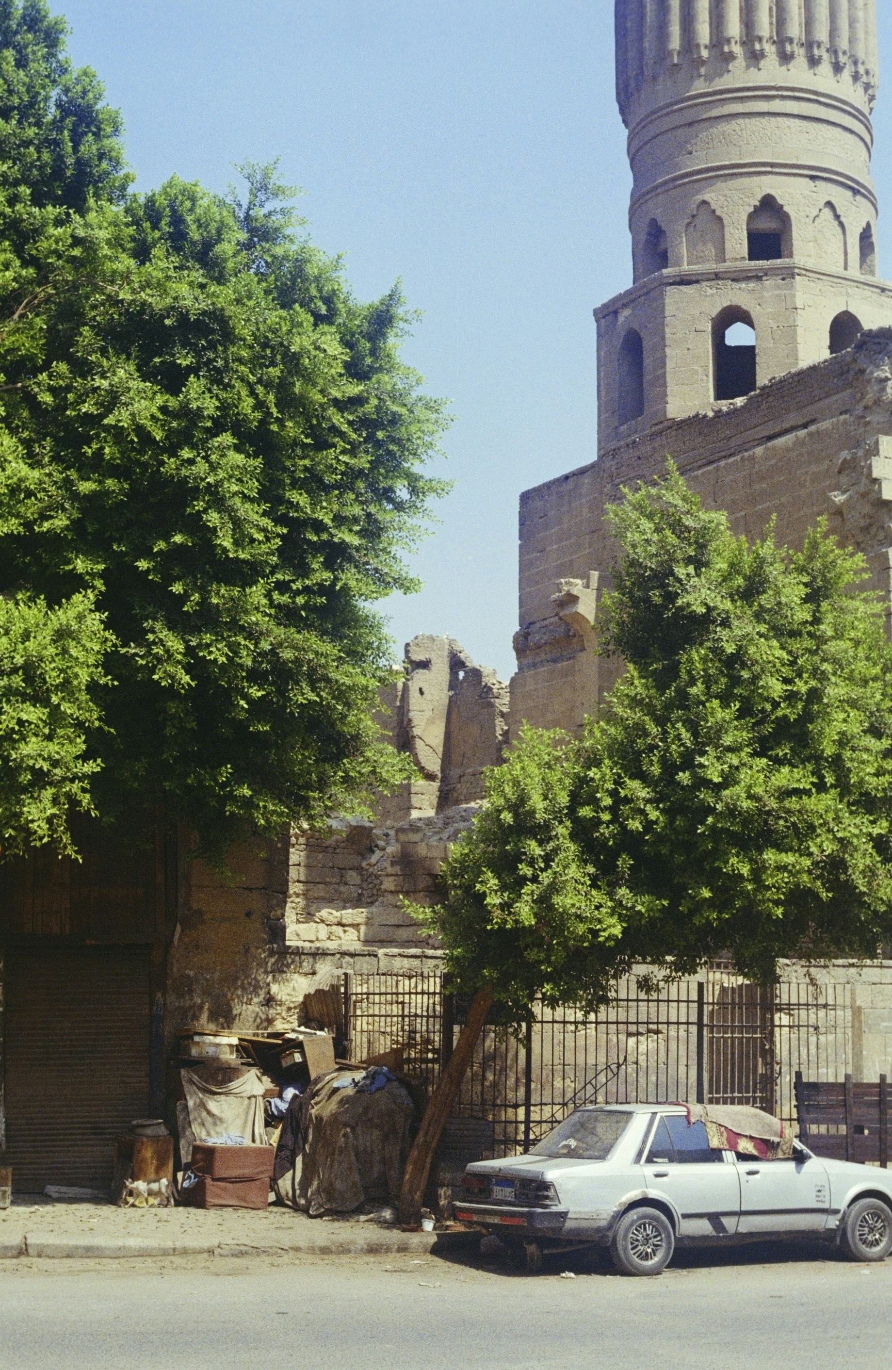 A silver car parked beside a stone minaret and trees in Cairo