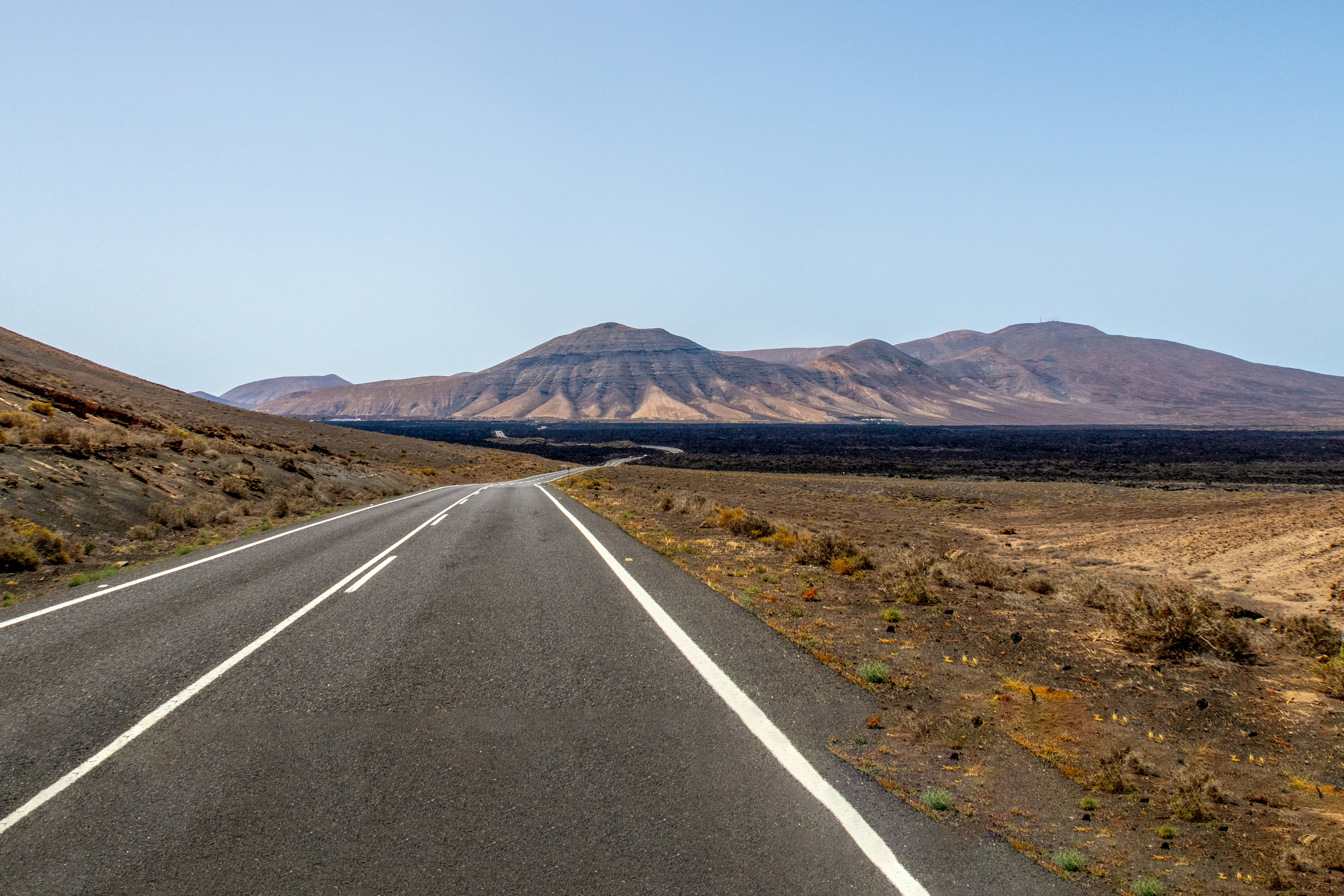 An asphalt road stretching through a volcanic landscape toward distant arid mountains