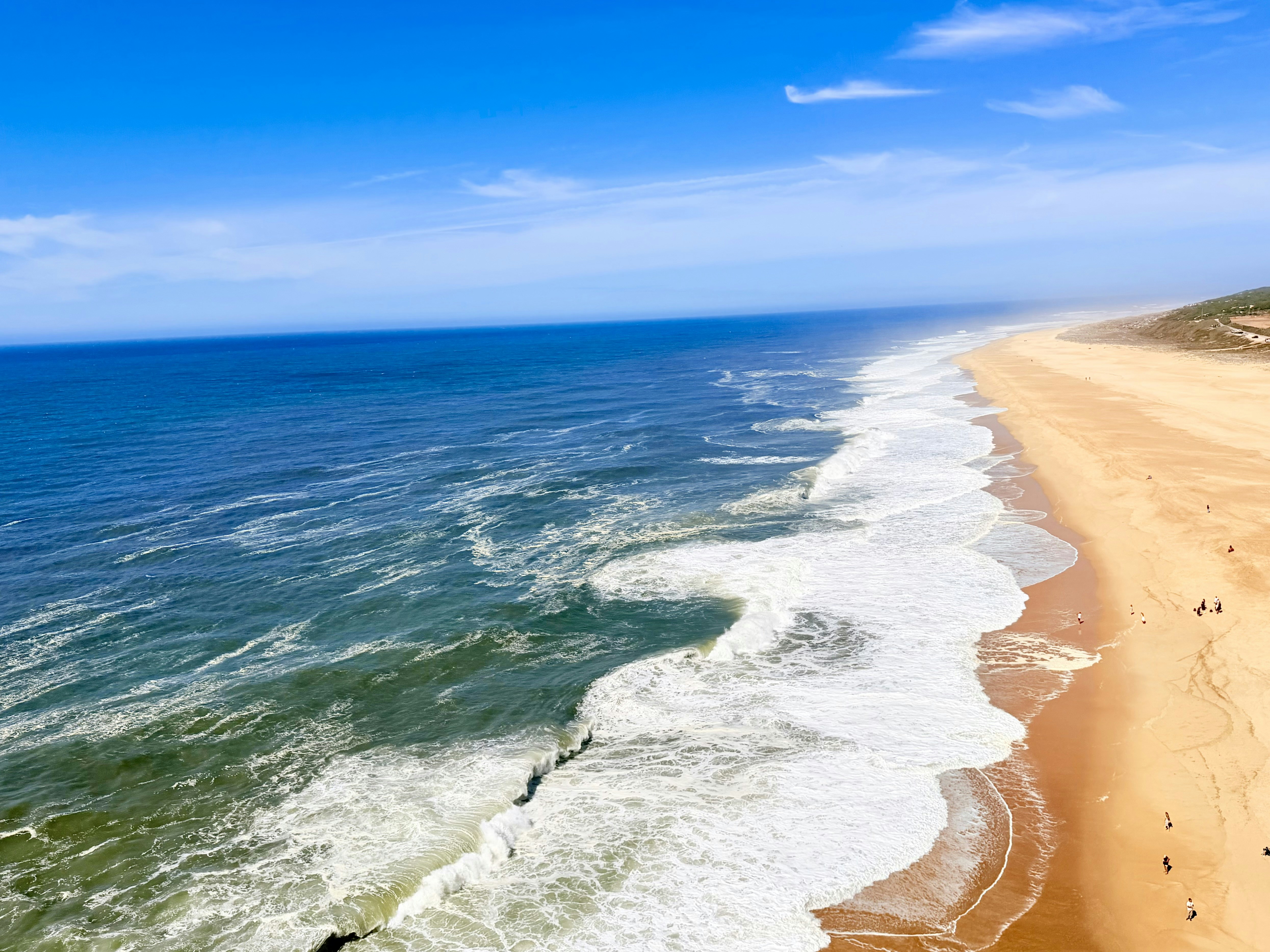 Aerial view of waves crashing onto a long sandy beach under a blue sky