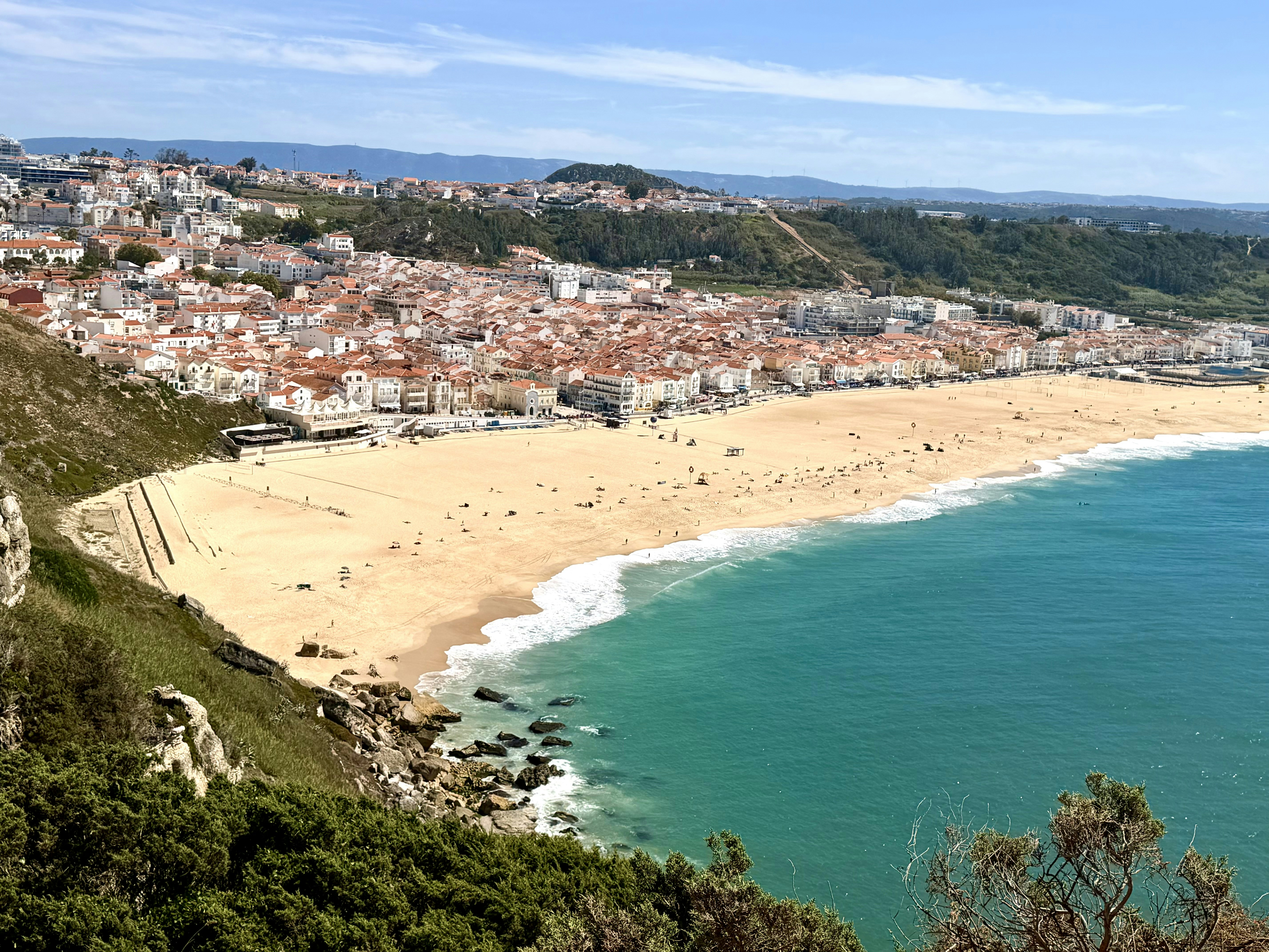 A sandy beach and turquoise water below the town of Nazaré in Portugal