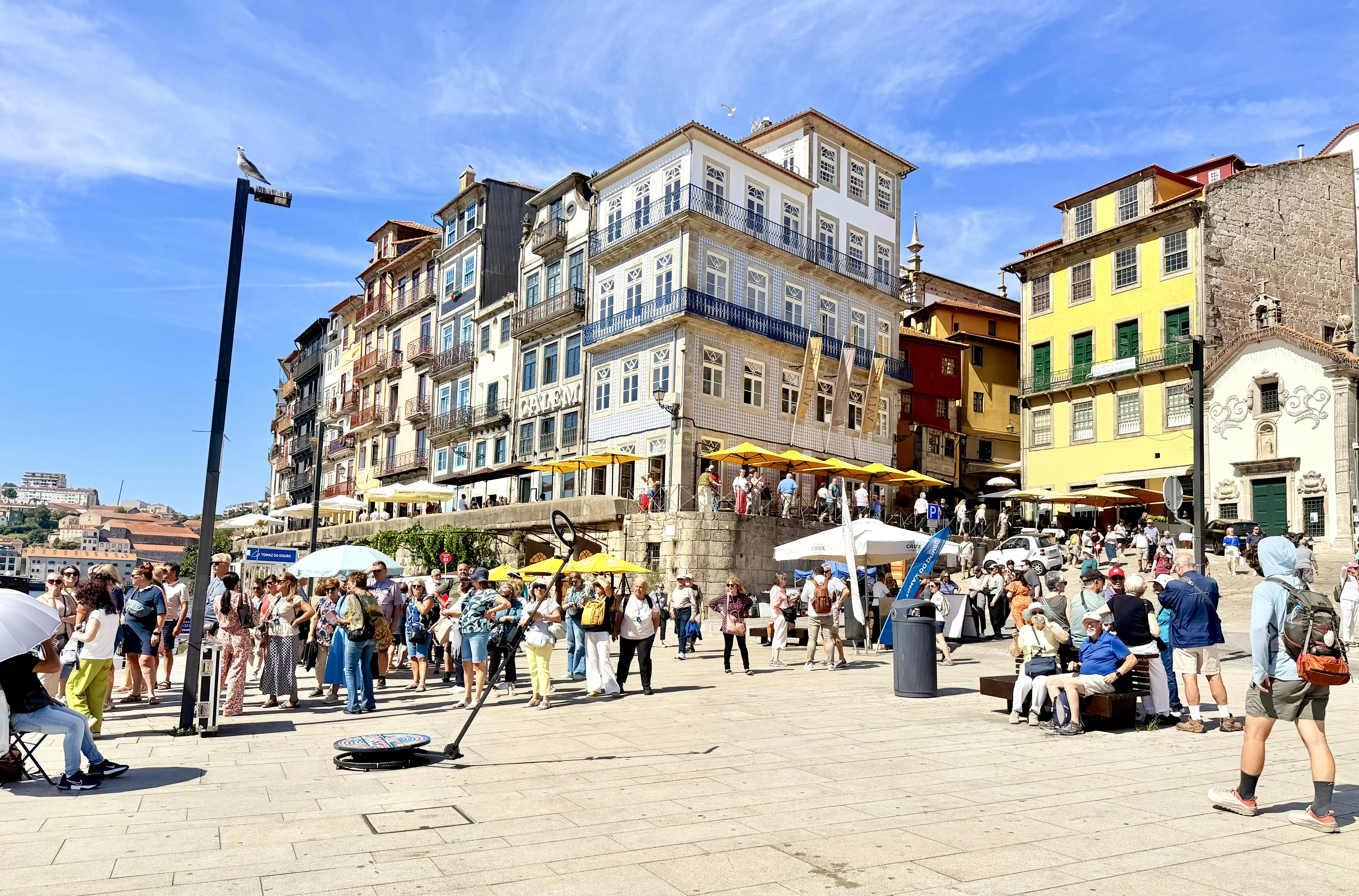 A crowd of people on a sunny riverside plaza in Porto with historic buildings