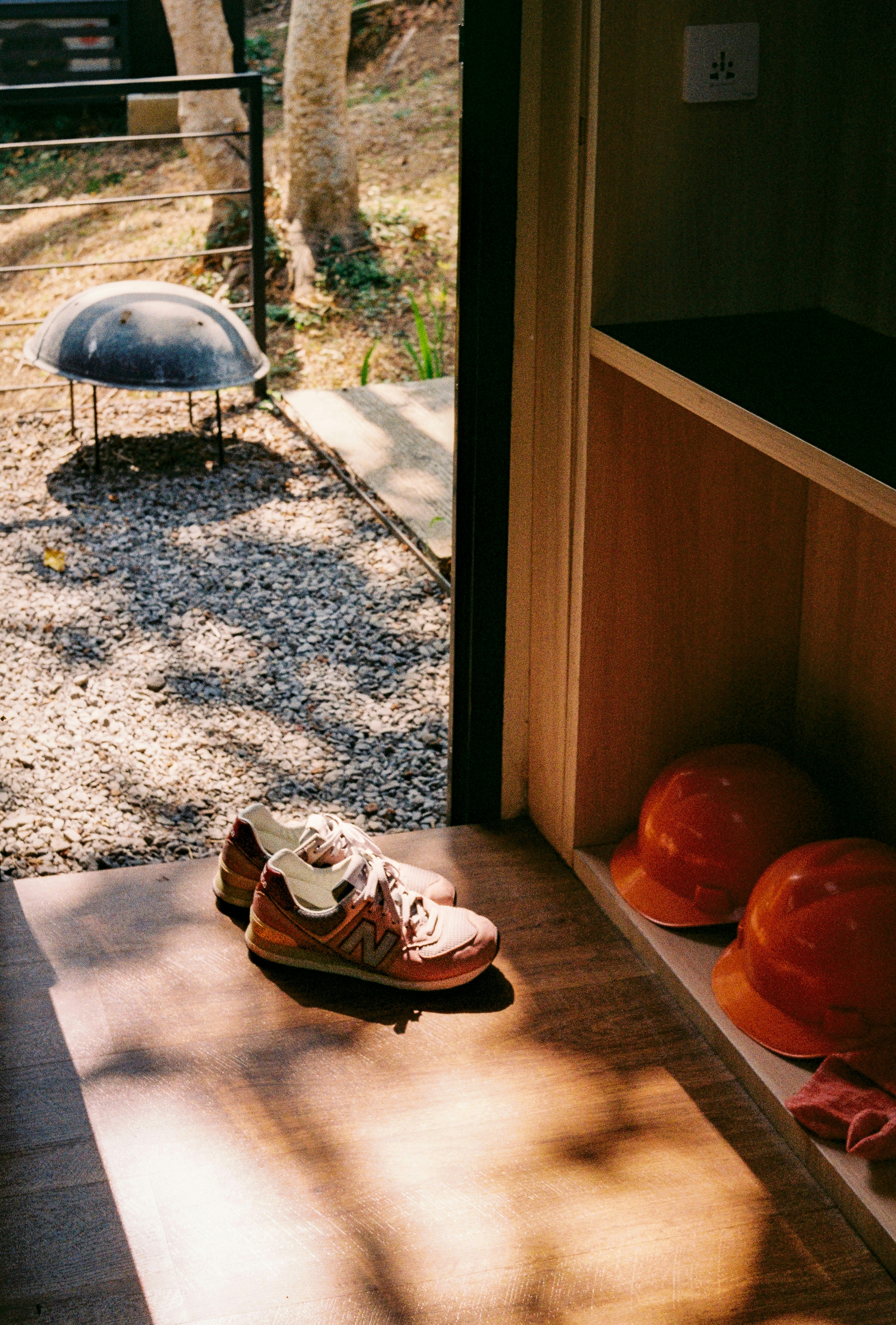 Sneakers and two orange hard hats on a wooden floor near an open doorway