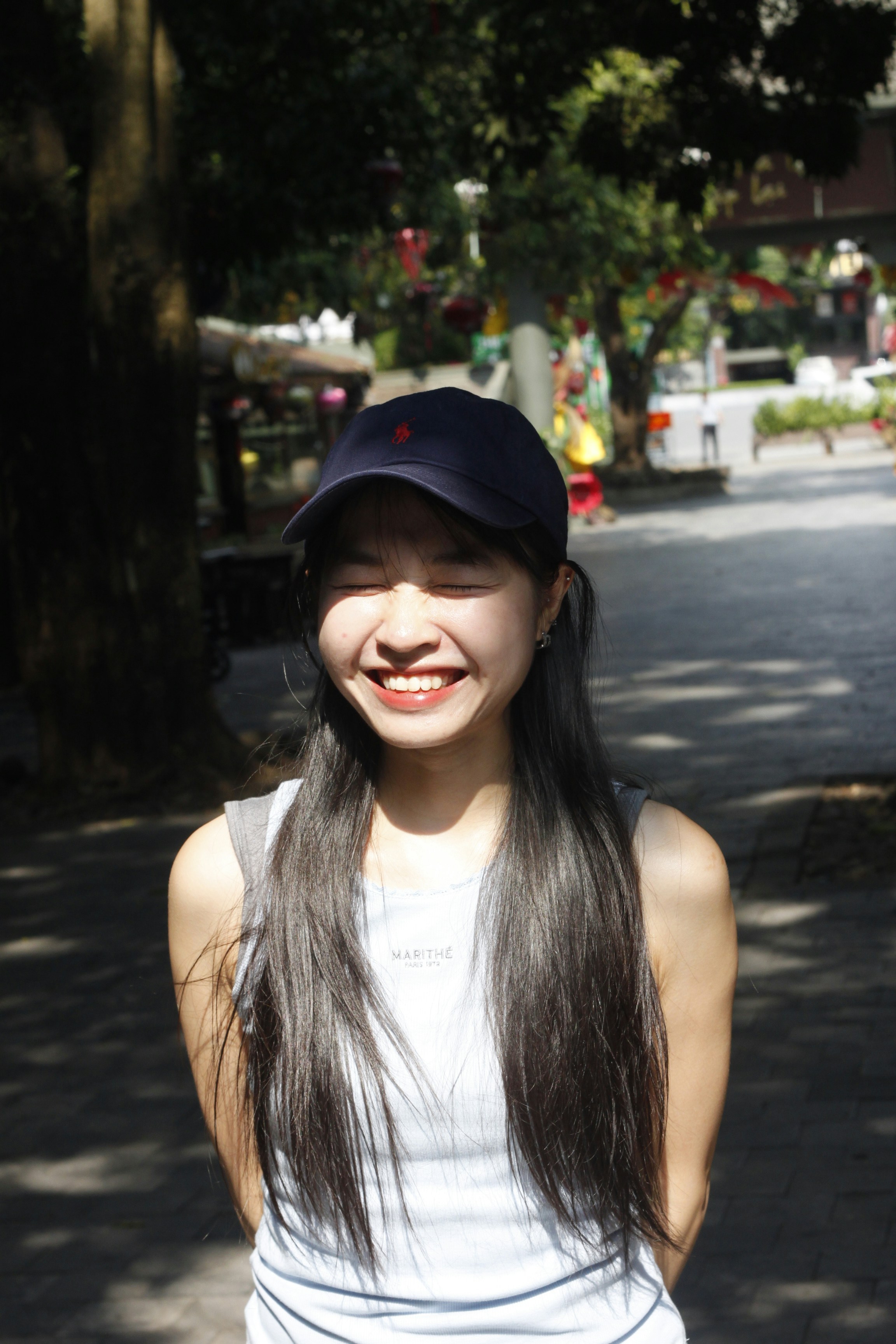 A smiling woman with long dark hair wearing a navy baseball cap outdoors