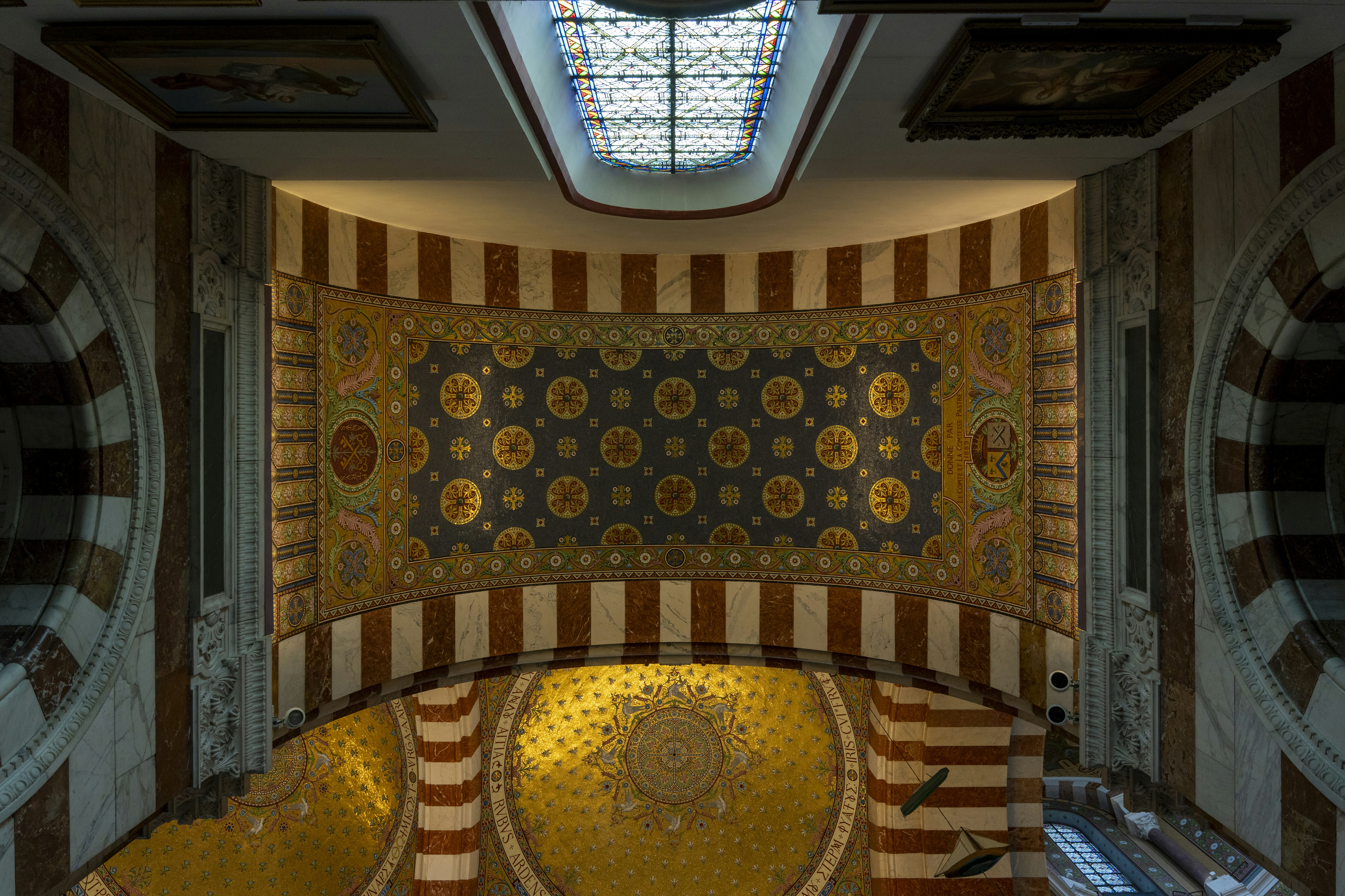 Ornate mosaic ceiling with gold patterns above striped marble arches in a cathedral
