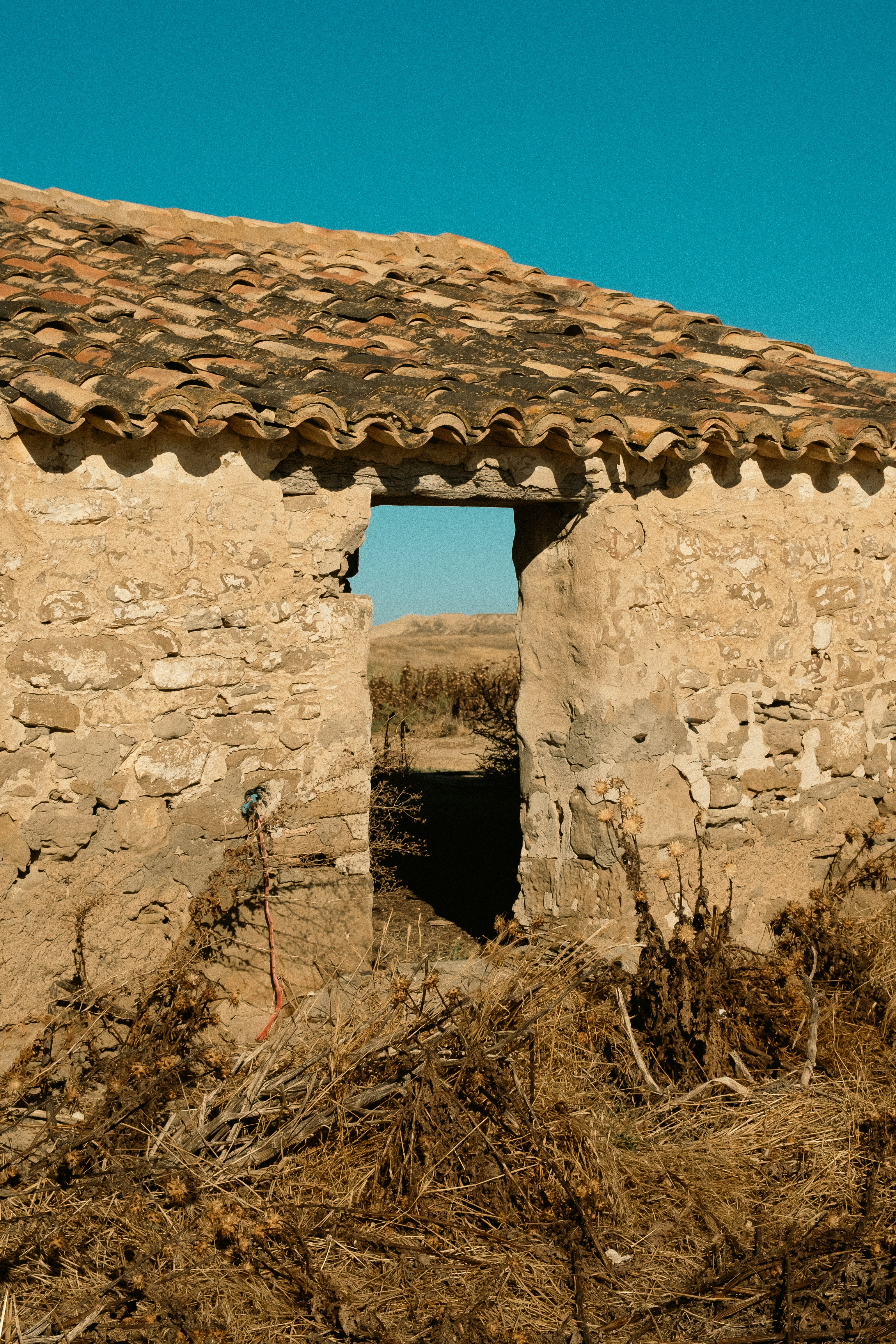 A stone wall with a terracotta tile roof and an open doorway