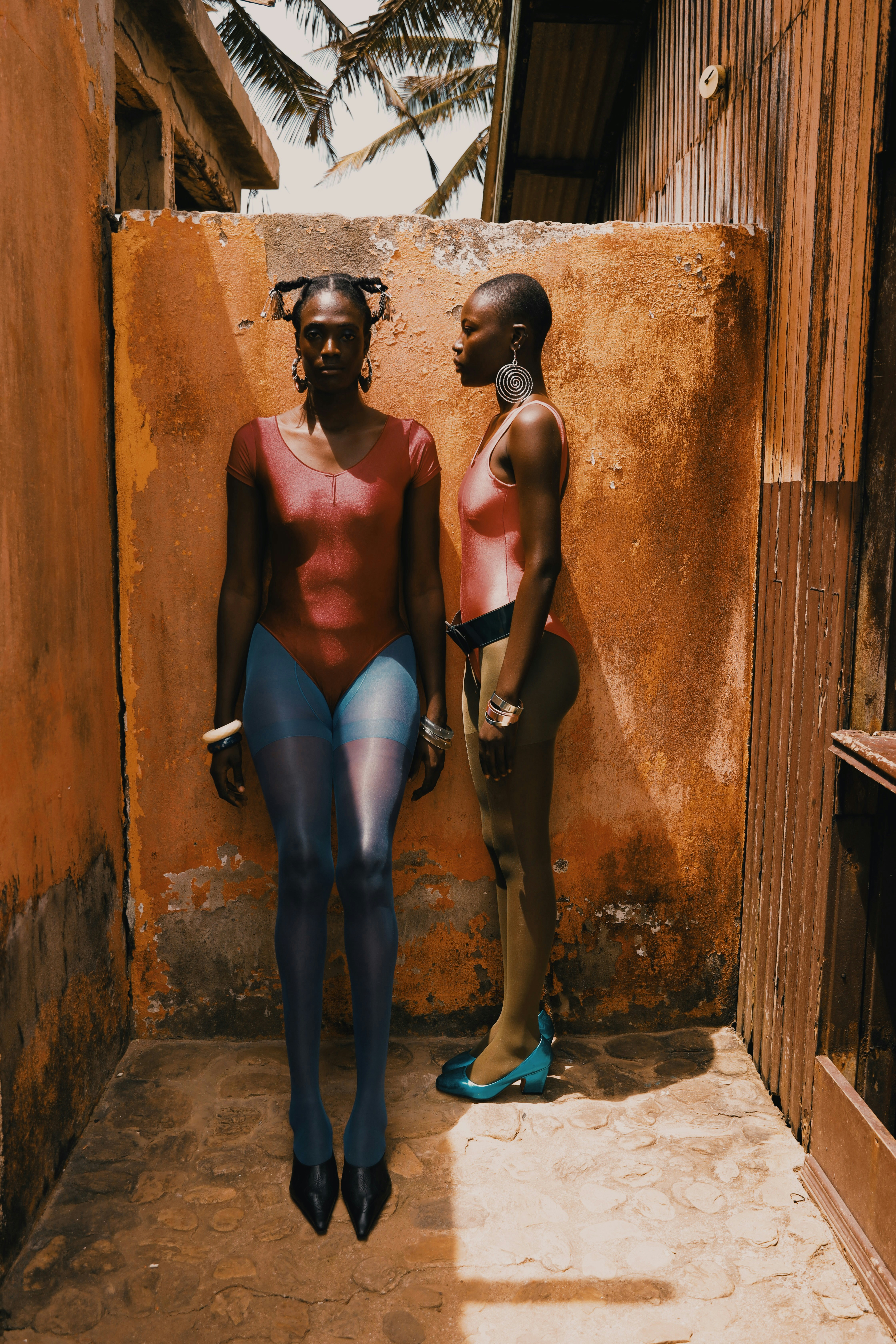 Two people in leotards and tights against a weathered orange wall