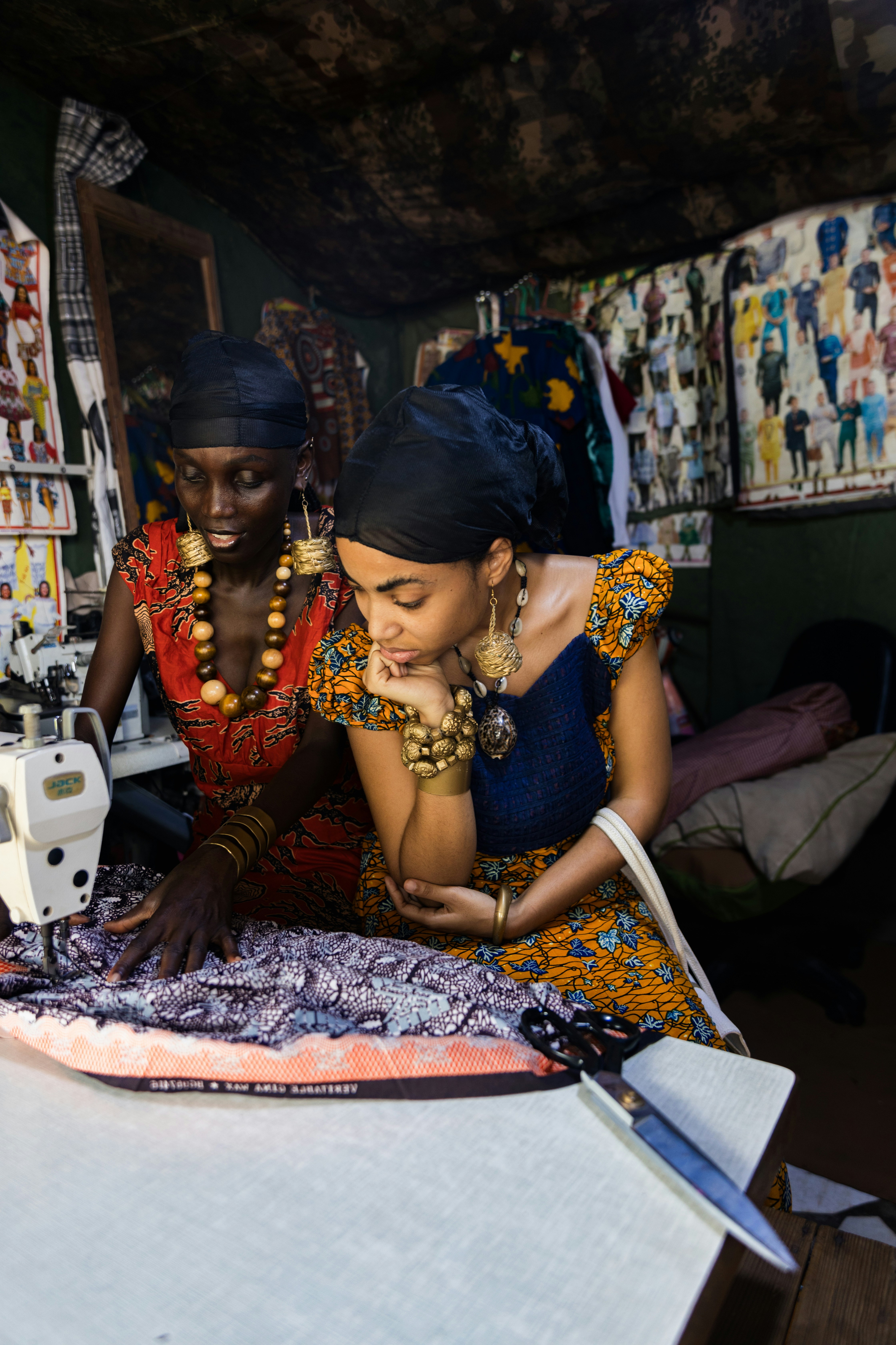 Two women in patterned dresses sewing fabric on a machine in a workshop