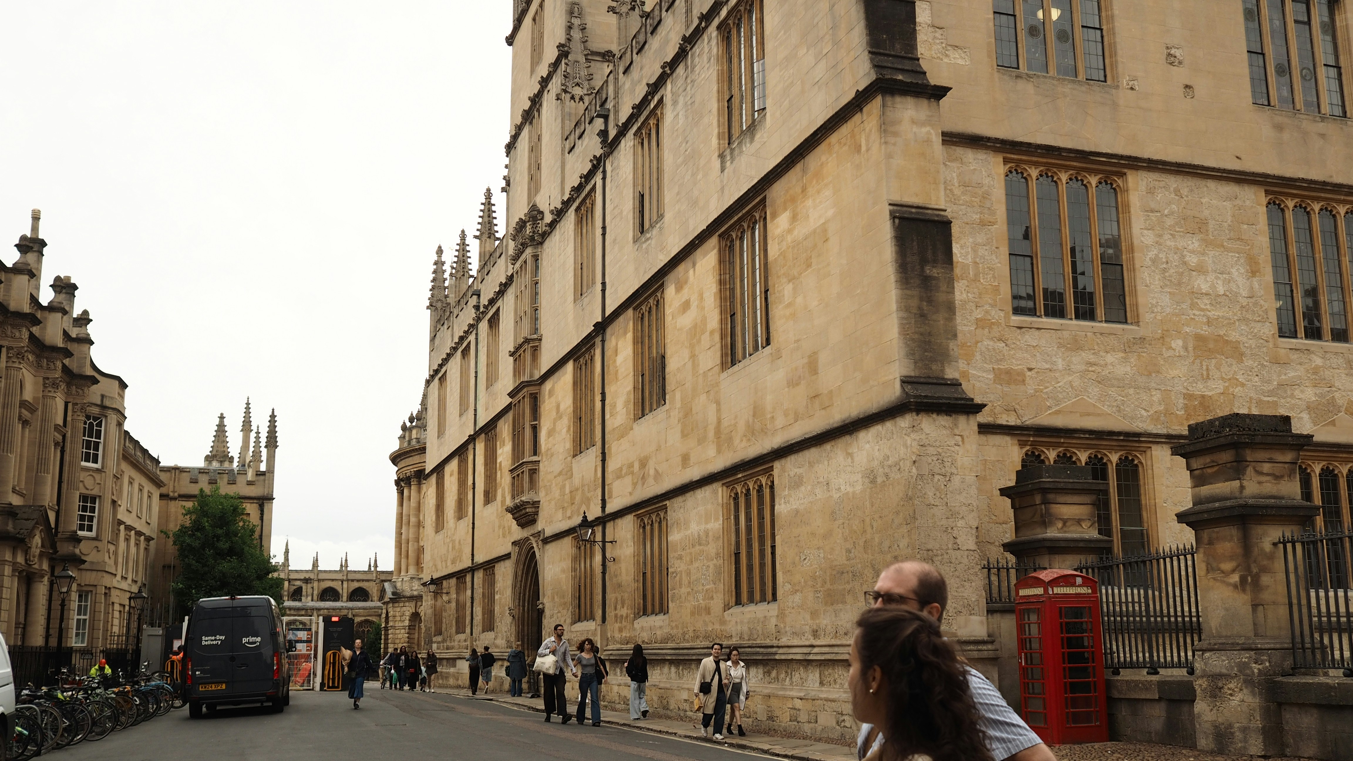 People walking on a street beside historic stone buildings and a red telephone box