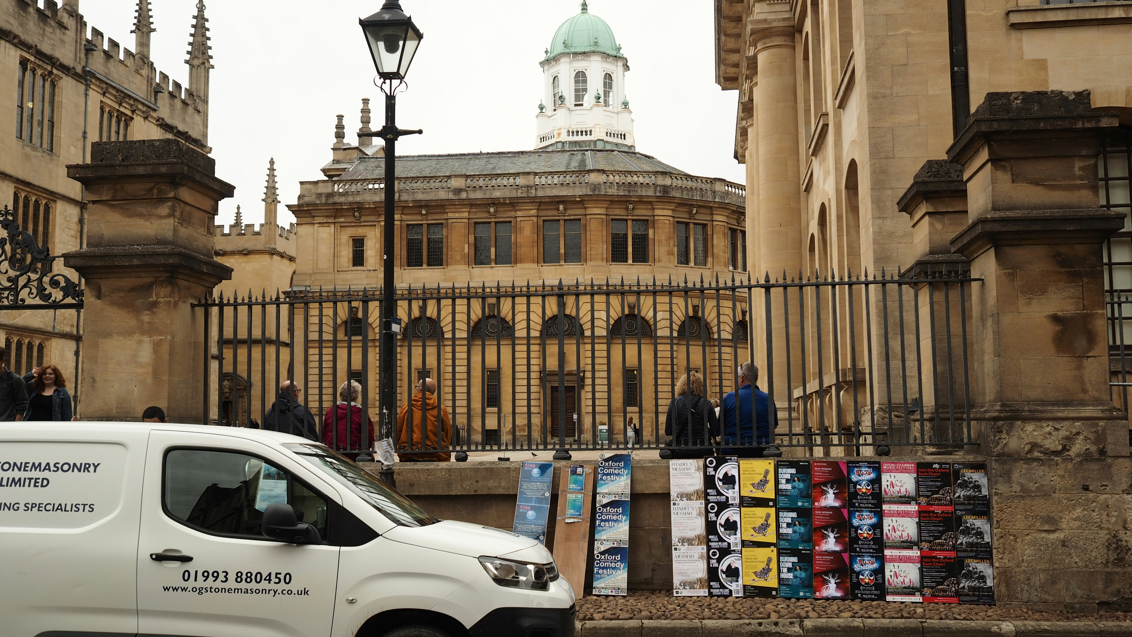 A white van parked before the Sheldonian Theatre in Oxford with event posters