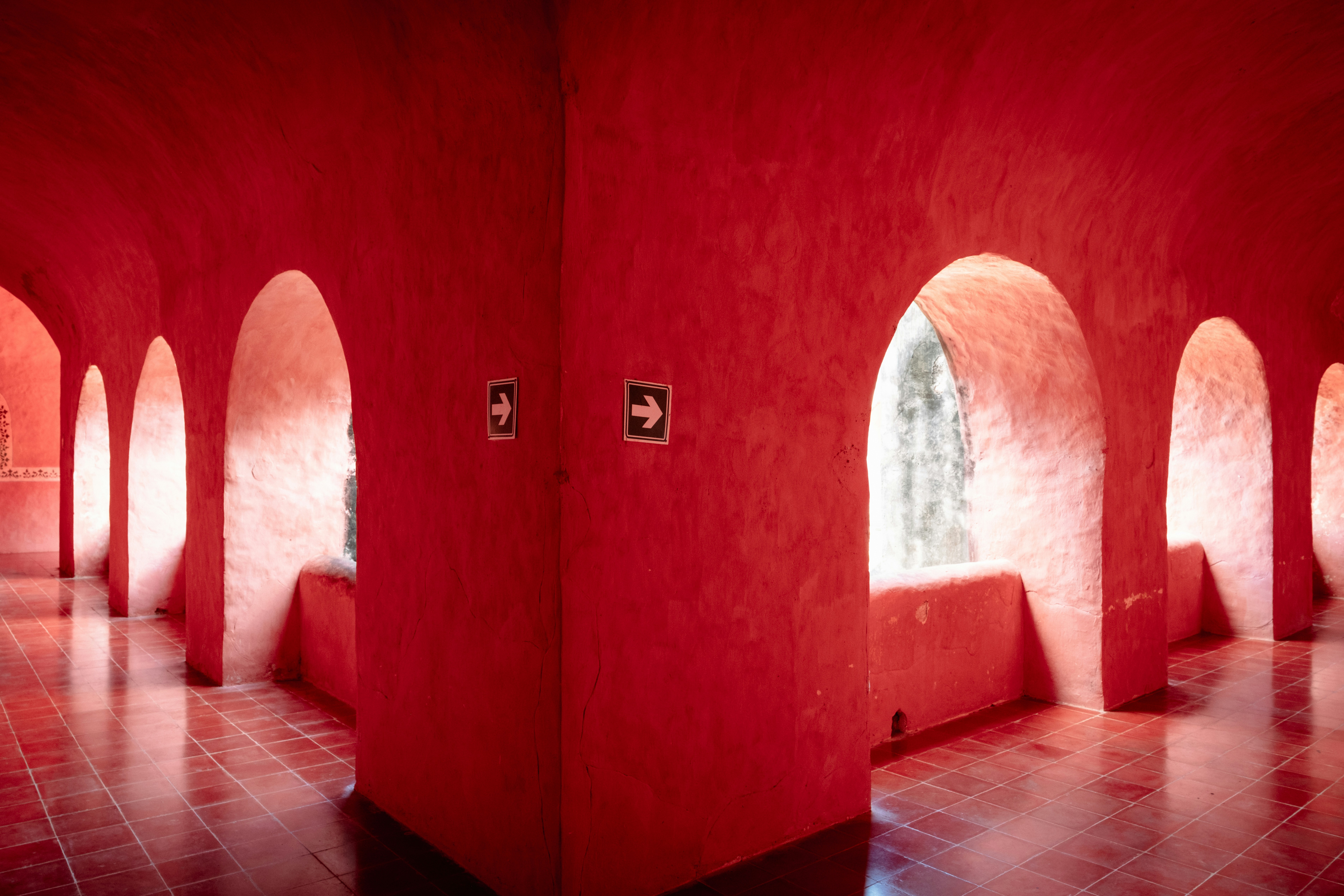 A bright red corridor with arched openings and directional arrow signs on the wall