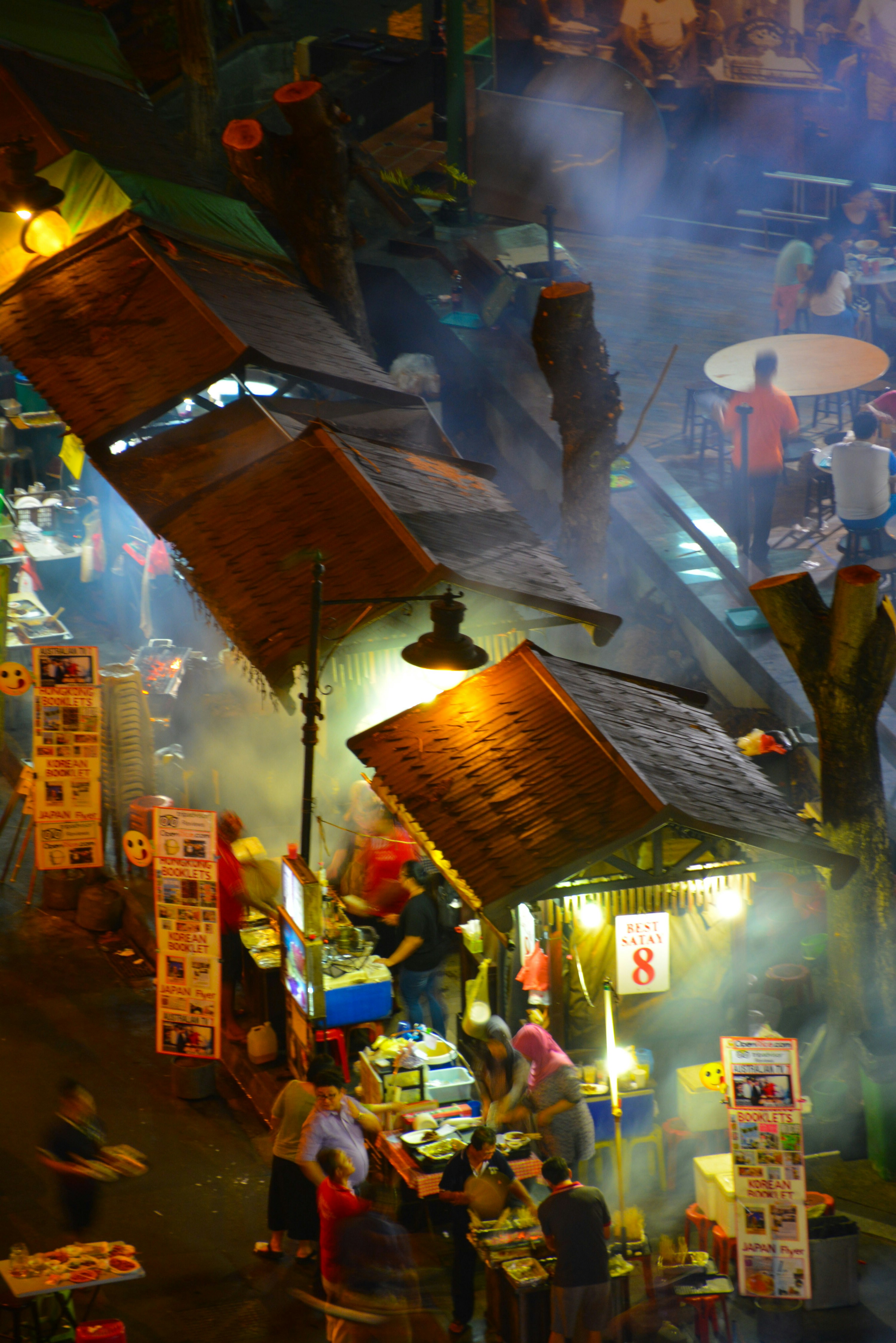Gente cocinando y comiendo en puestos de comida al aire libre en un mercado nocturno lleno de humo
