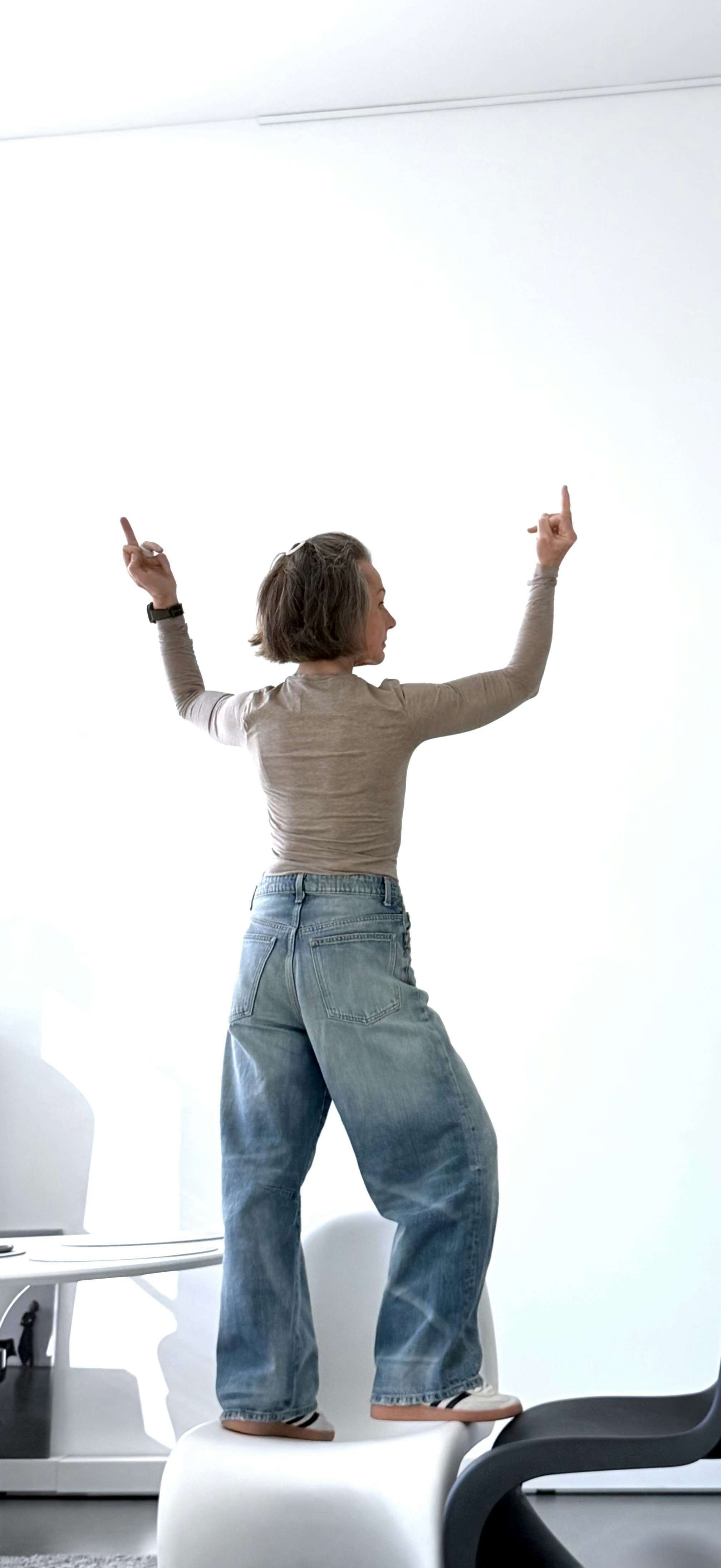 A woman in a beige long-sleeved shirt and jeans standing on a white chair