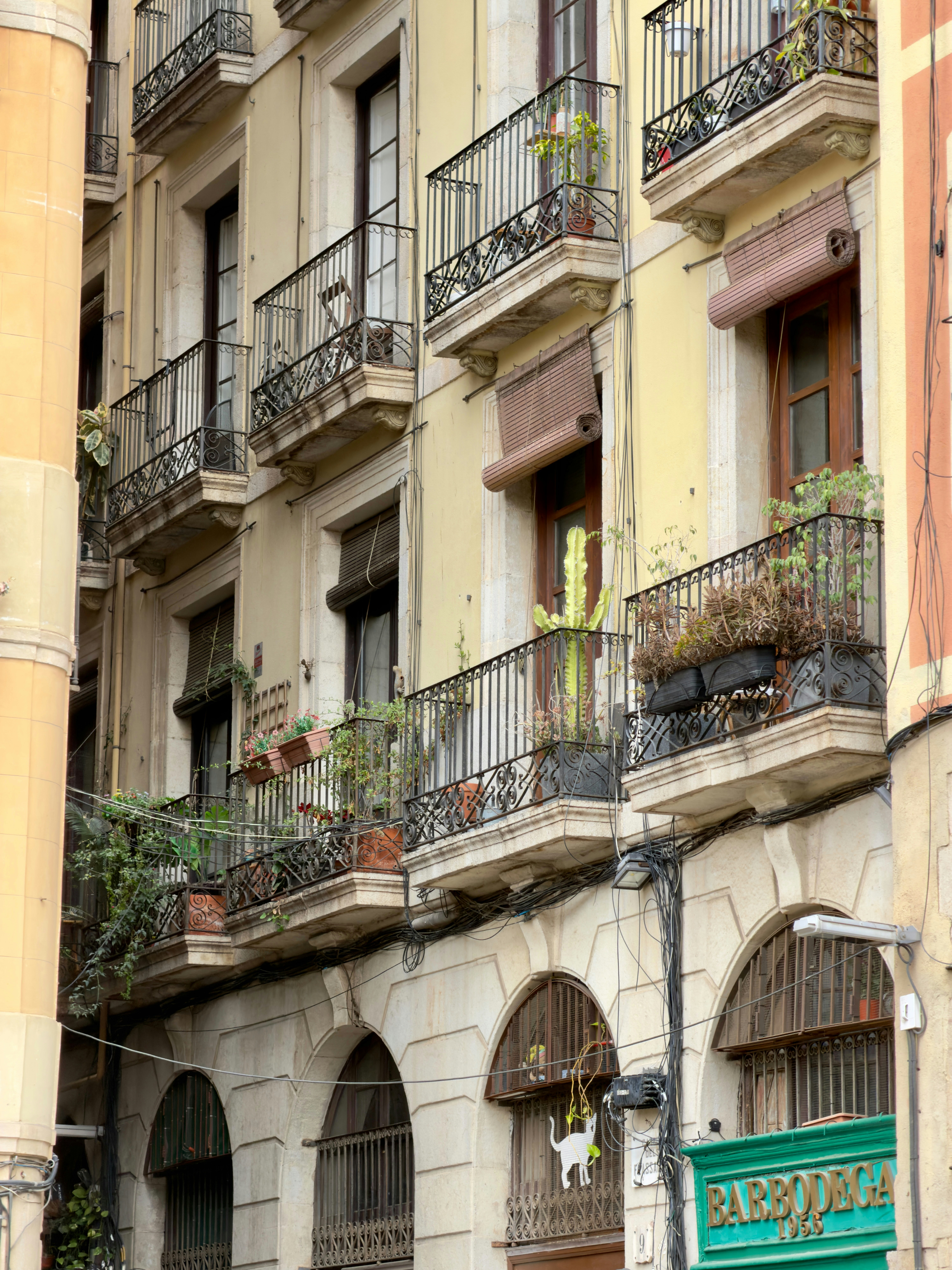 A yellow apartment building with wrought iron balconies and potted plants in Barcelona