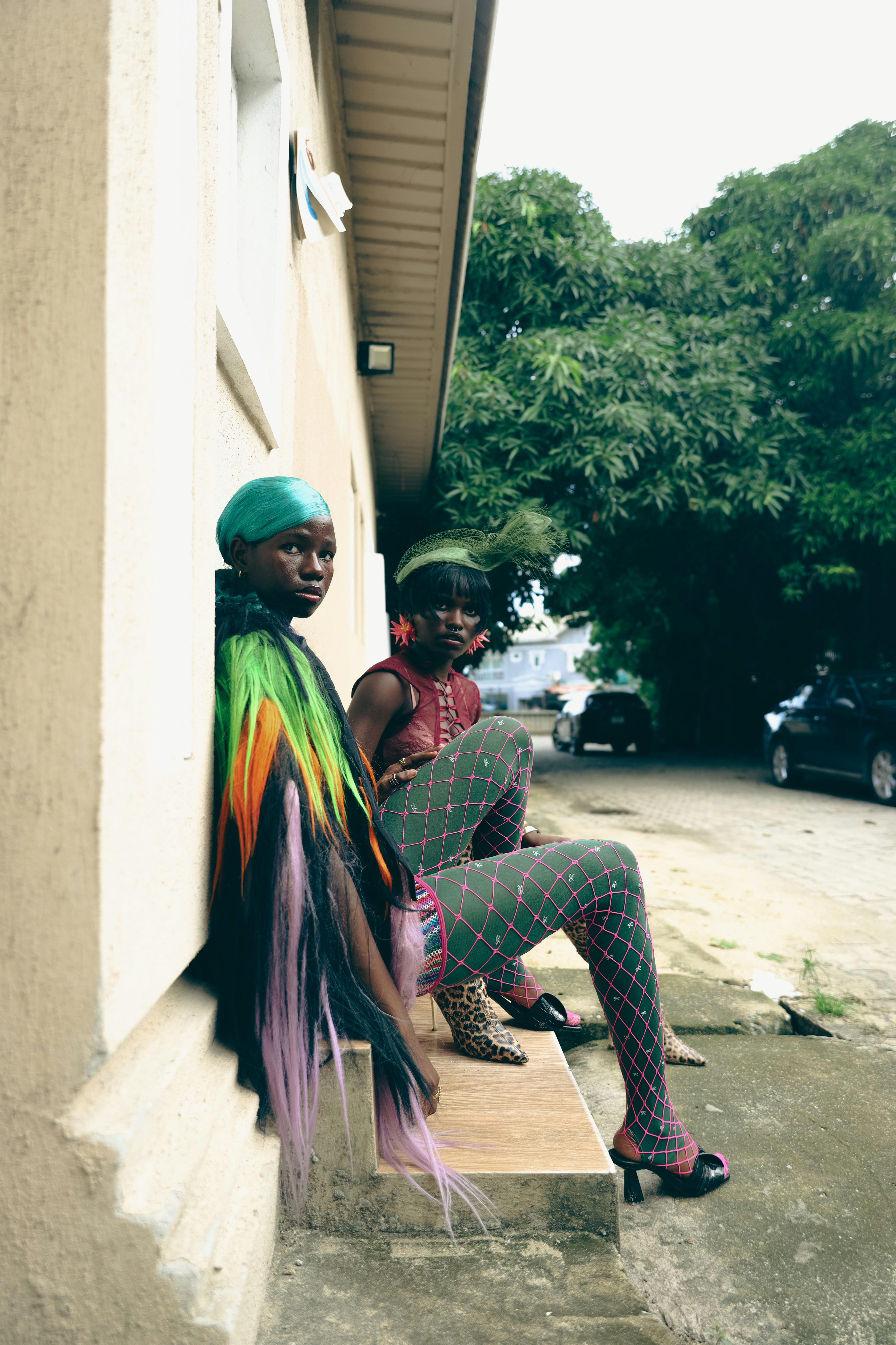 Two people in colorful fashion sitting on steps against a beige building wall