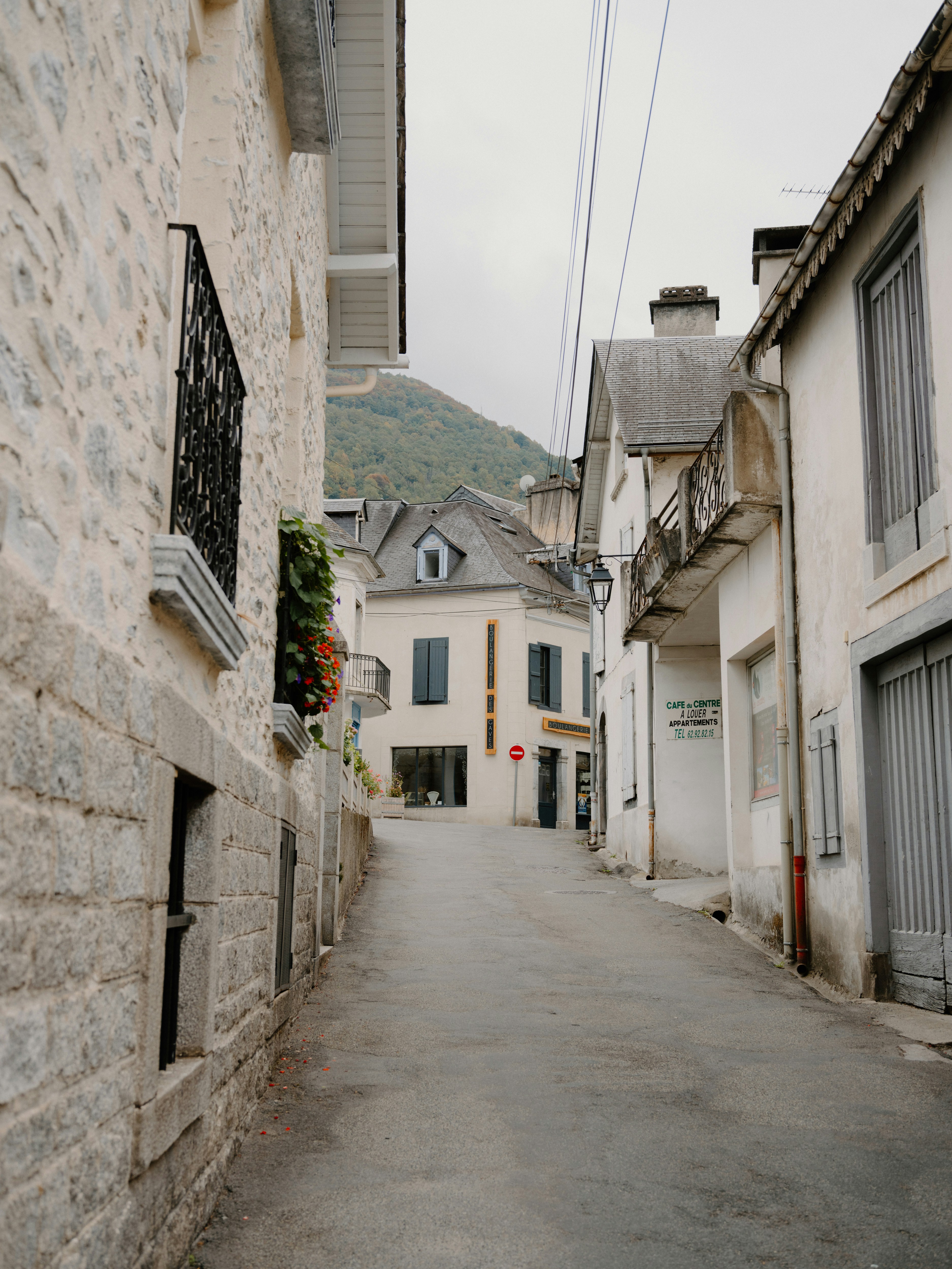 A narrow street between stone buildings leading toward a mountain in a French village
