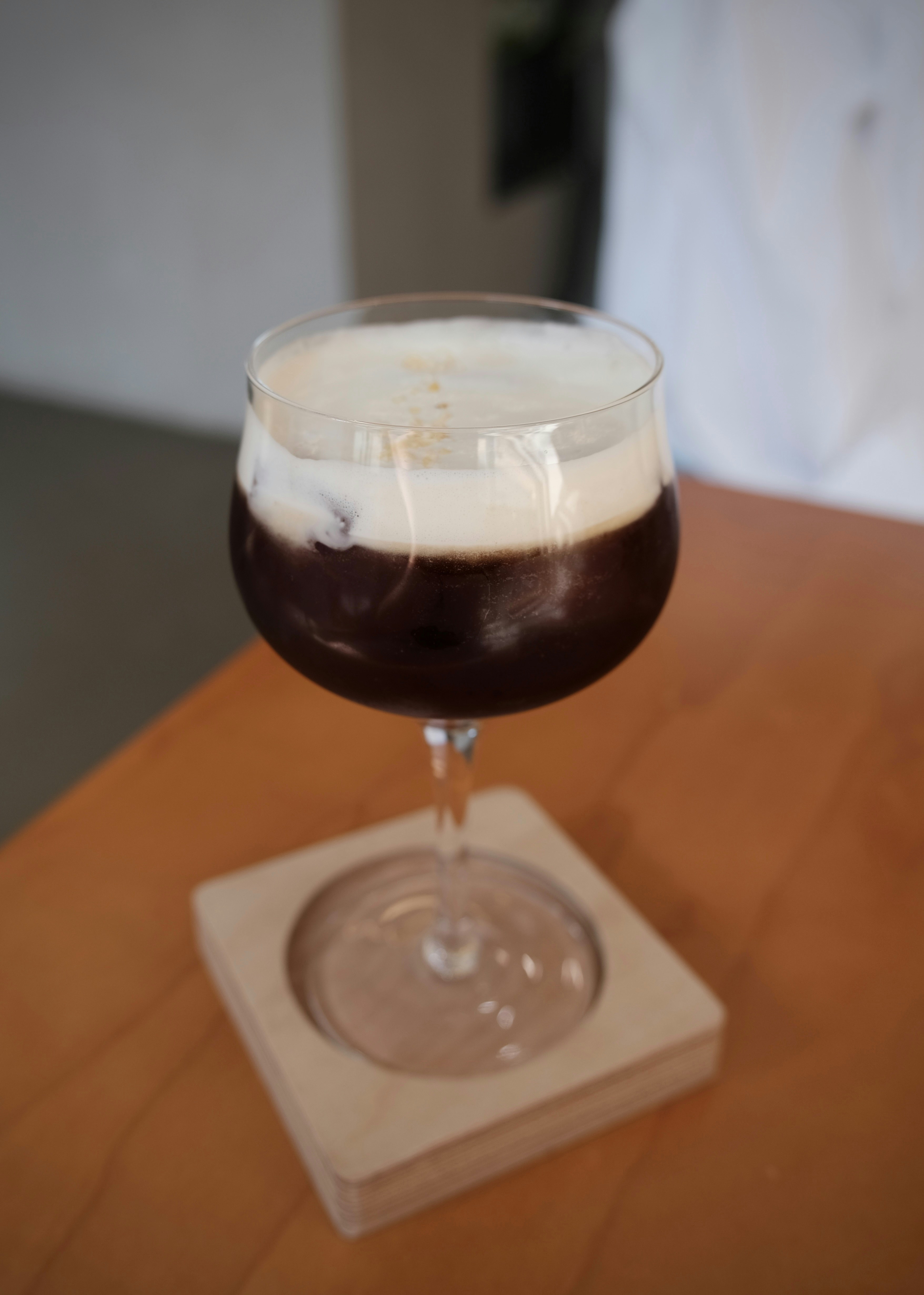 An espresso martini with thick white foam in a stemmed glass on a coaster