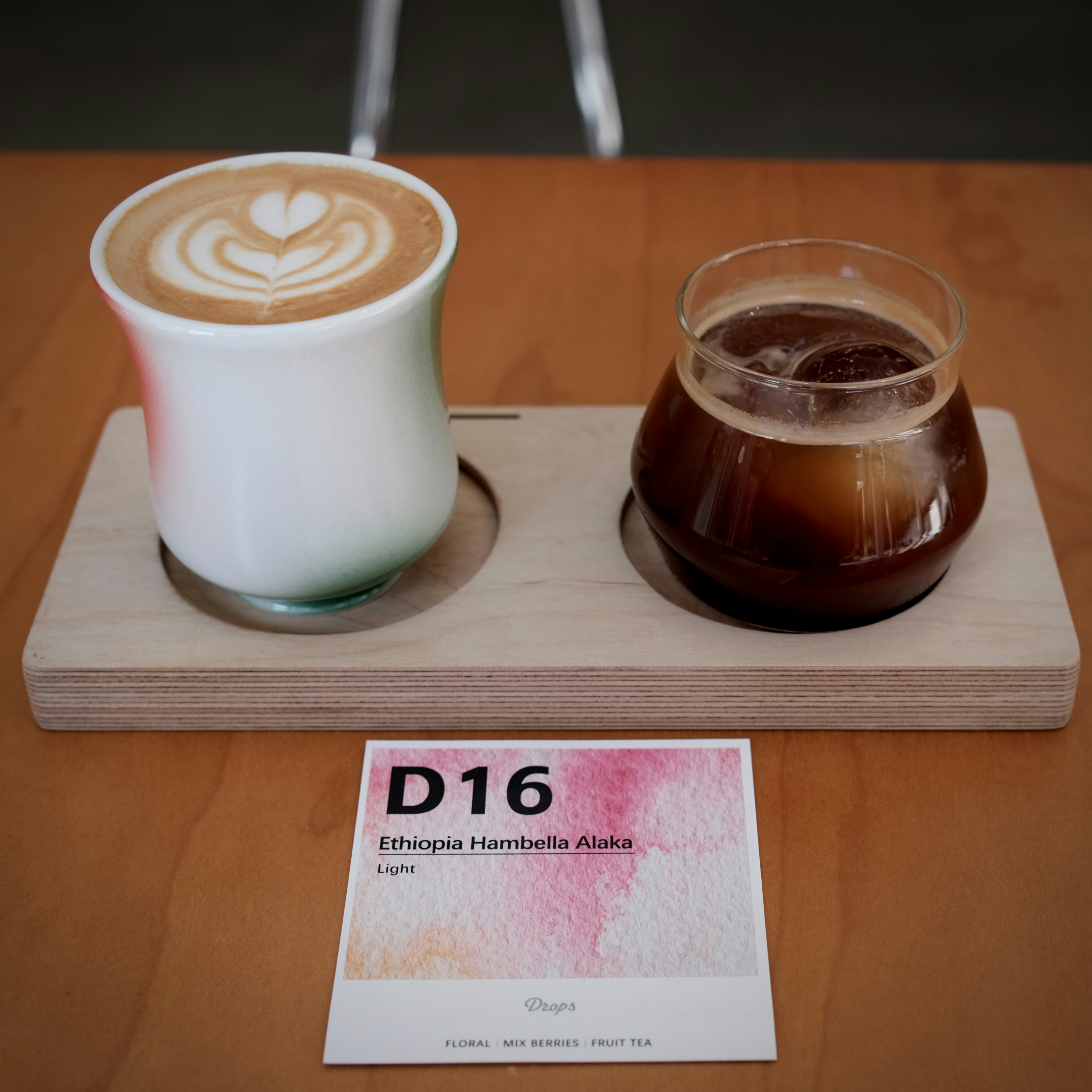 A latte with heart latte art and iced coffee on a wooden serving tray
