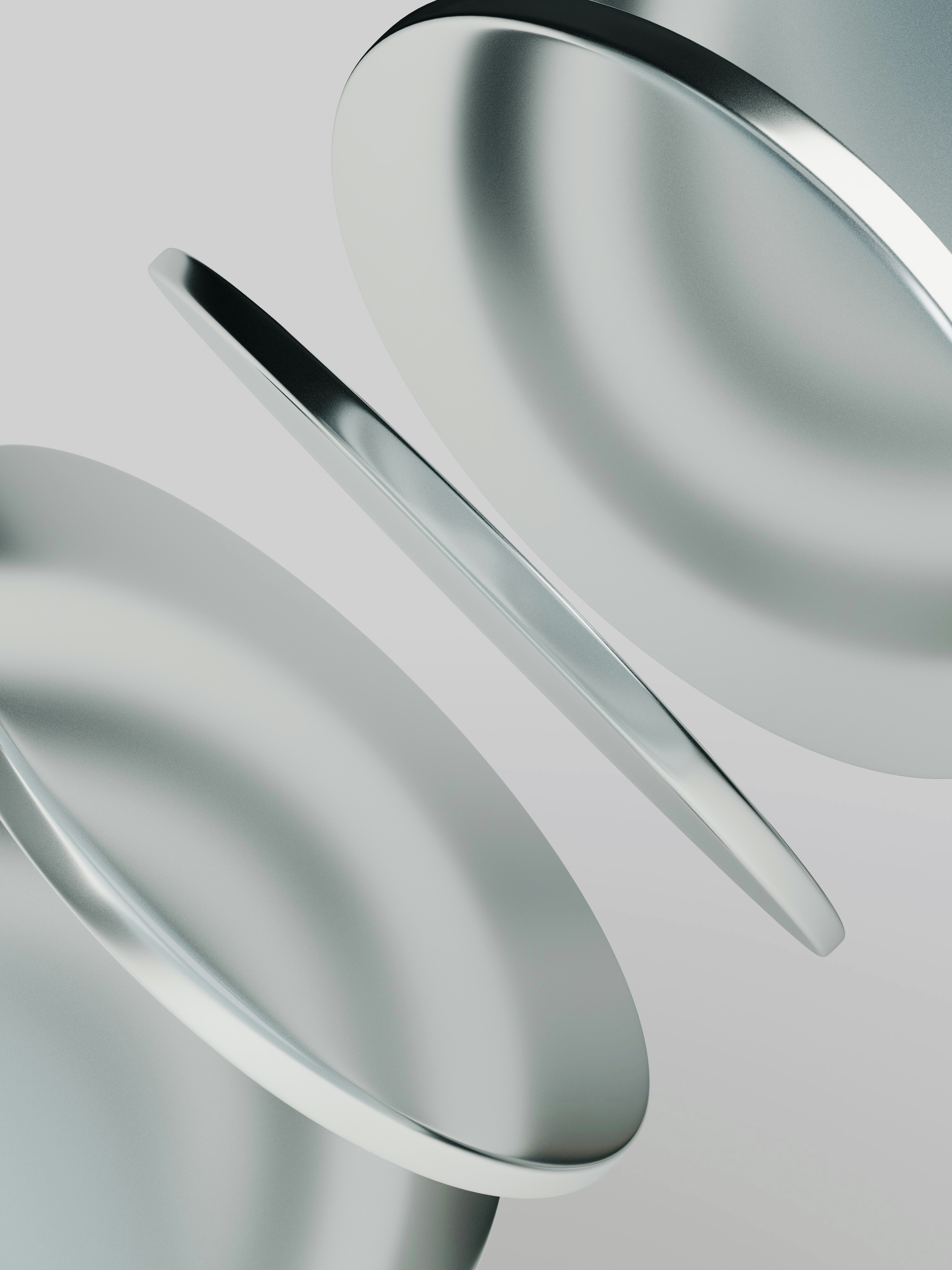 Three smooth metallic discs floating at an angle against a light grey background