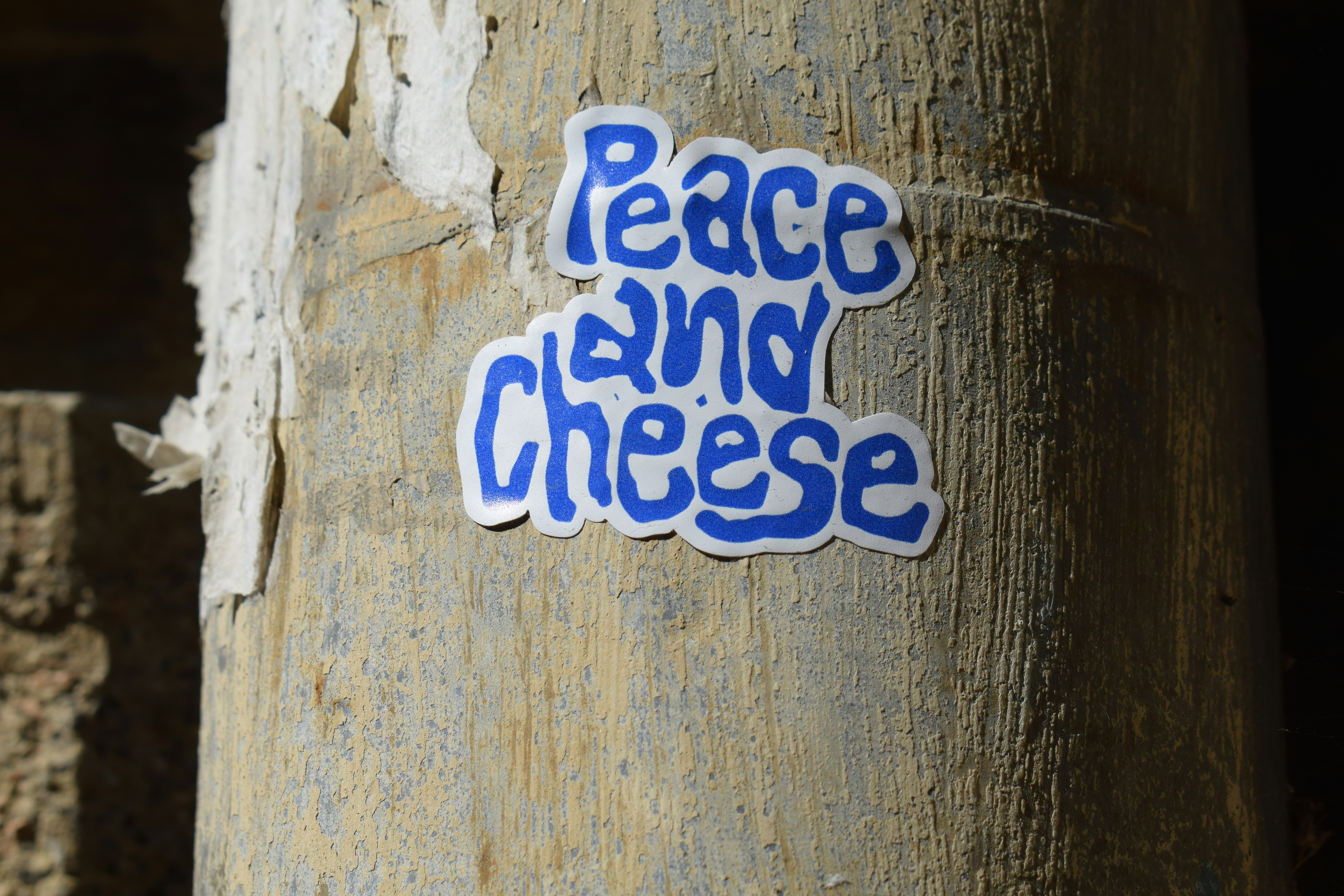 A blue sticker reading Peace and Cheese on a weathered concrete pillar