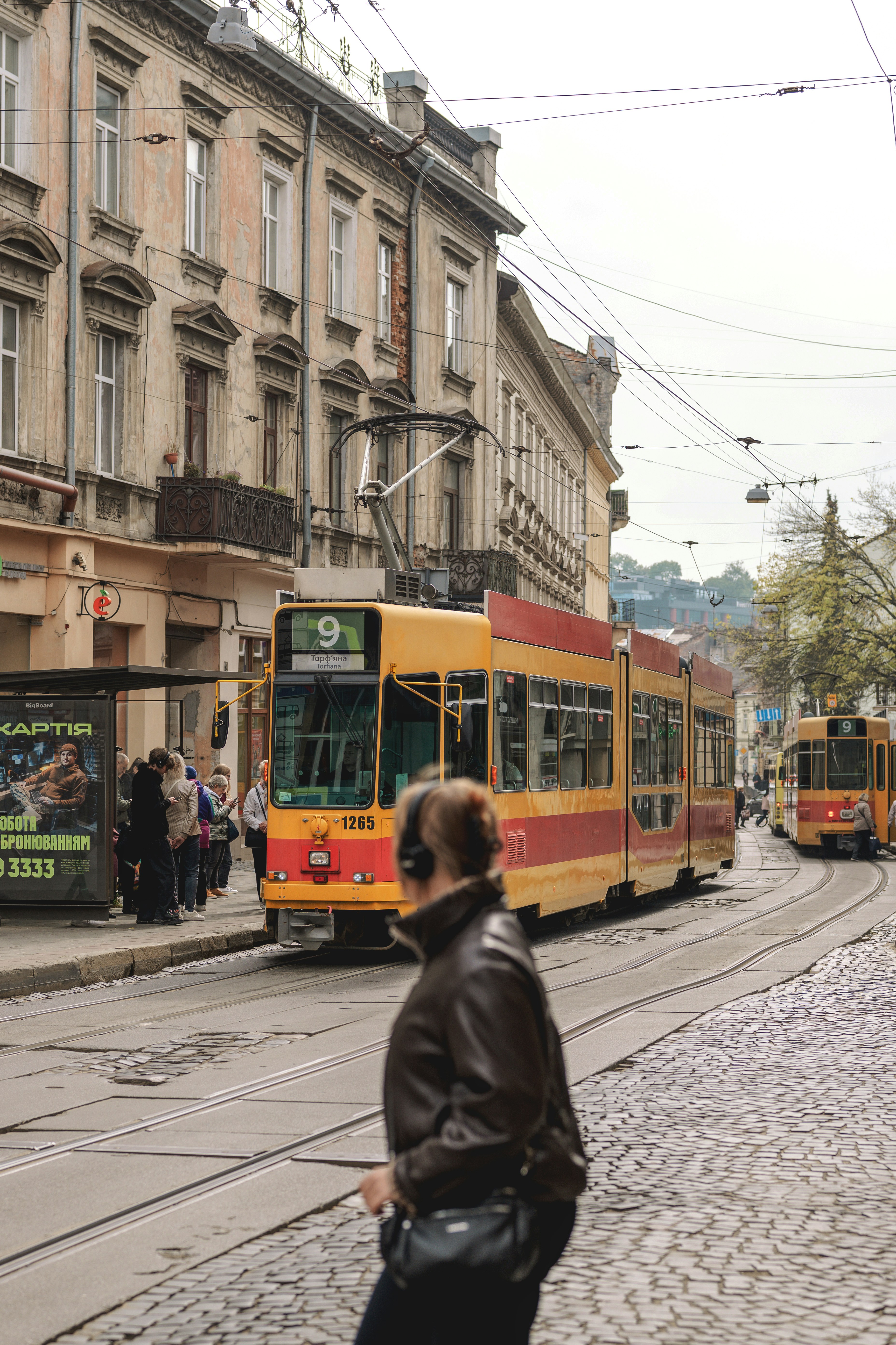 Un tranvía amarillo en una parada de la ciudad con gente esperando en la acera
