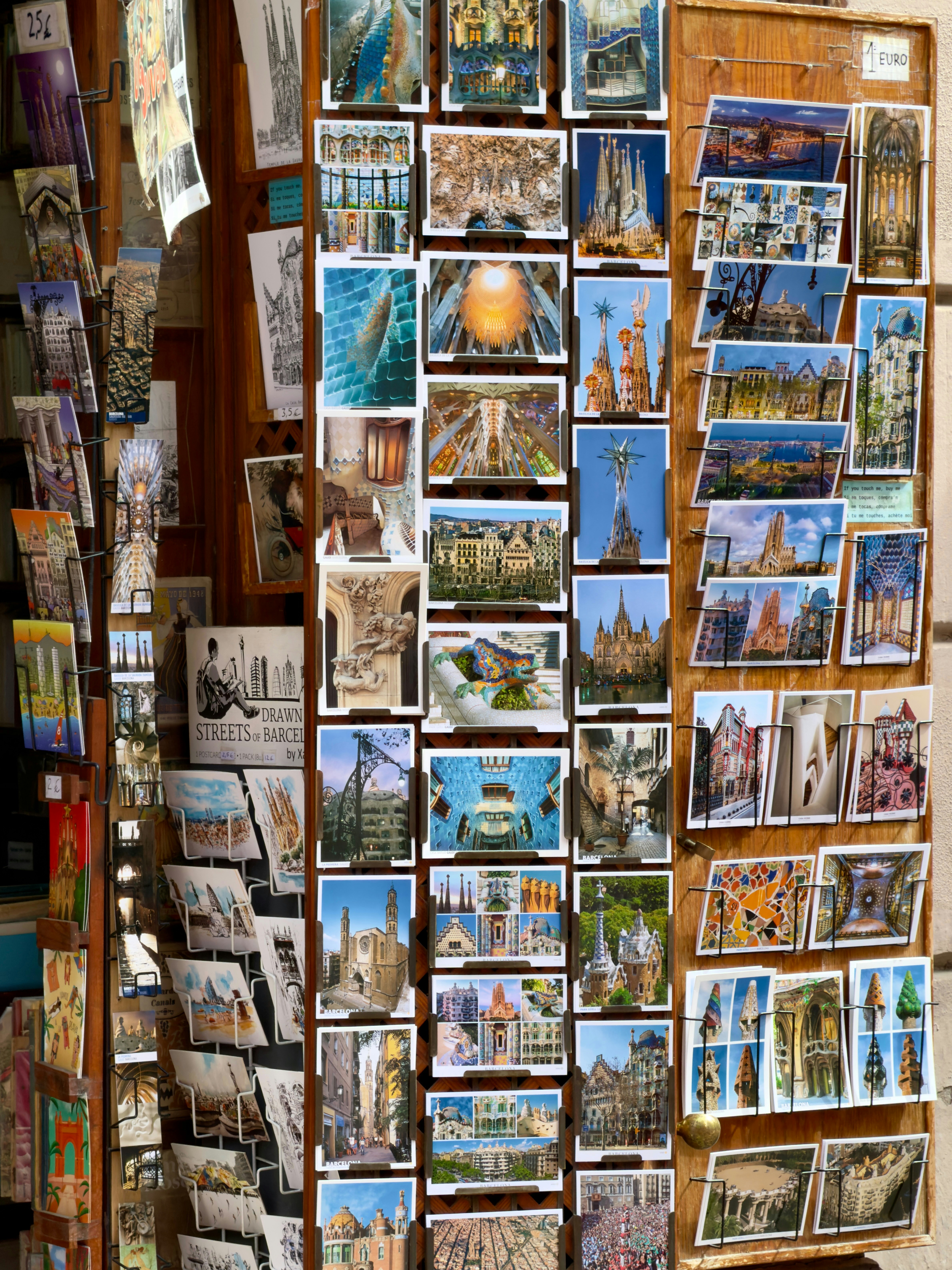 A wooden display rack filled with numerous postcards of landmarks in Barcelona, Spain