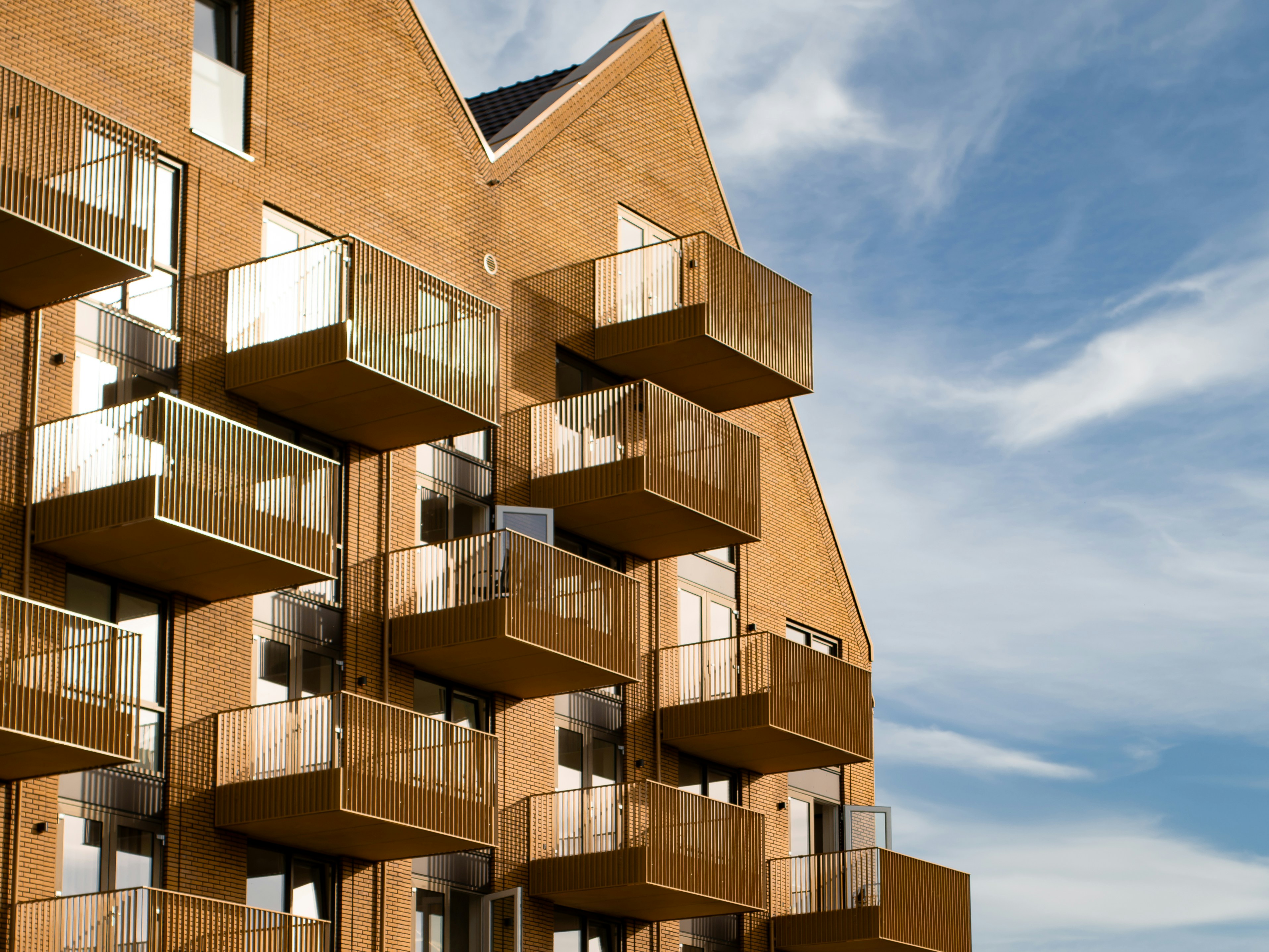 Un immeuble moderne en brique avec des balcons superposés sous un ciel bleu