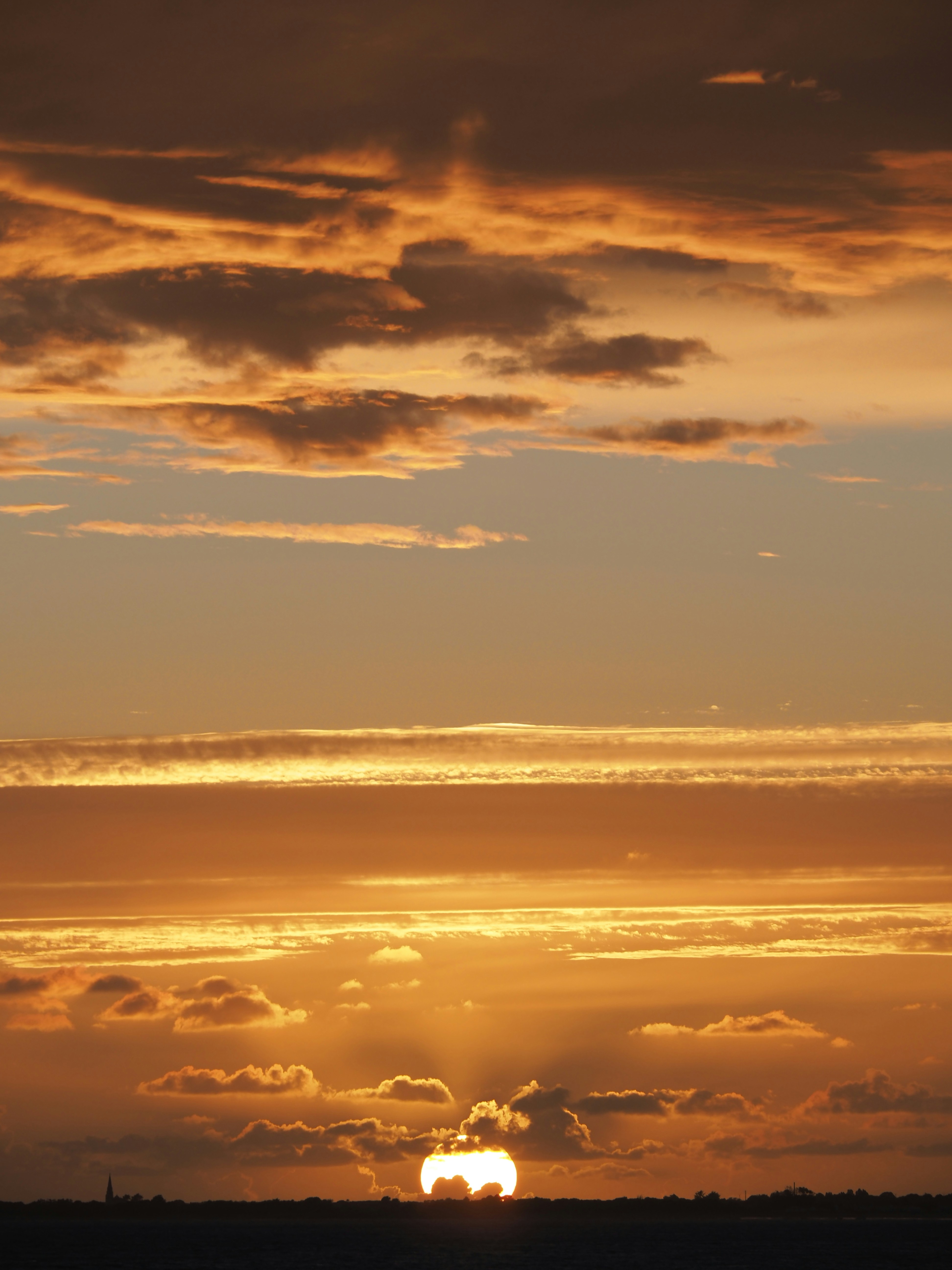 Low sun glowing behind dark clouds in a warm orange sky