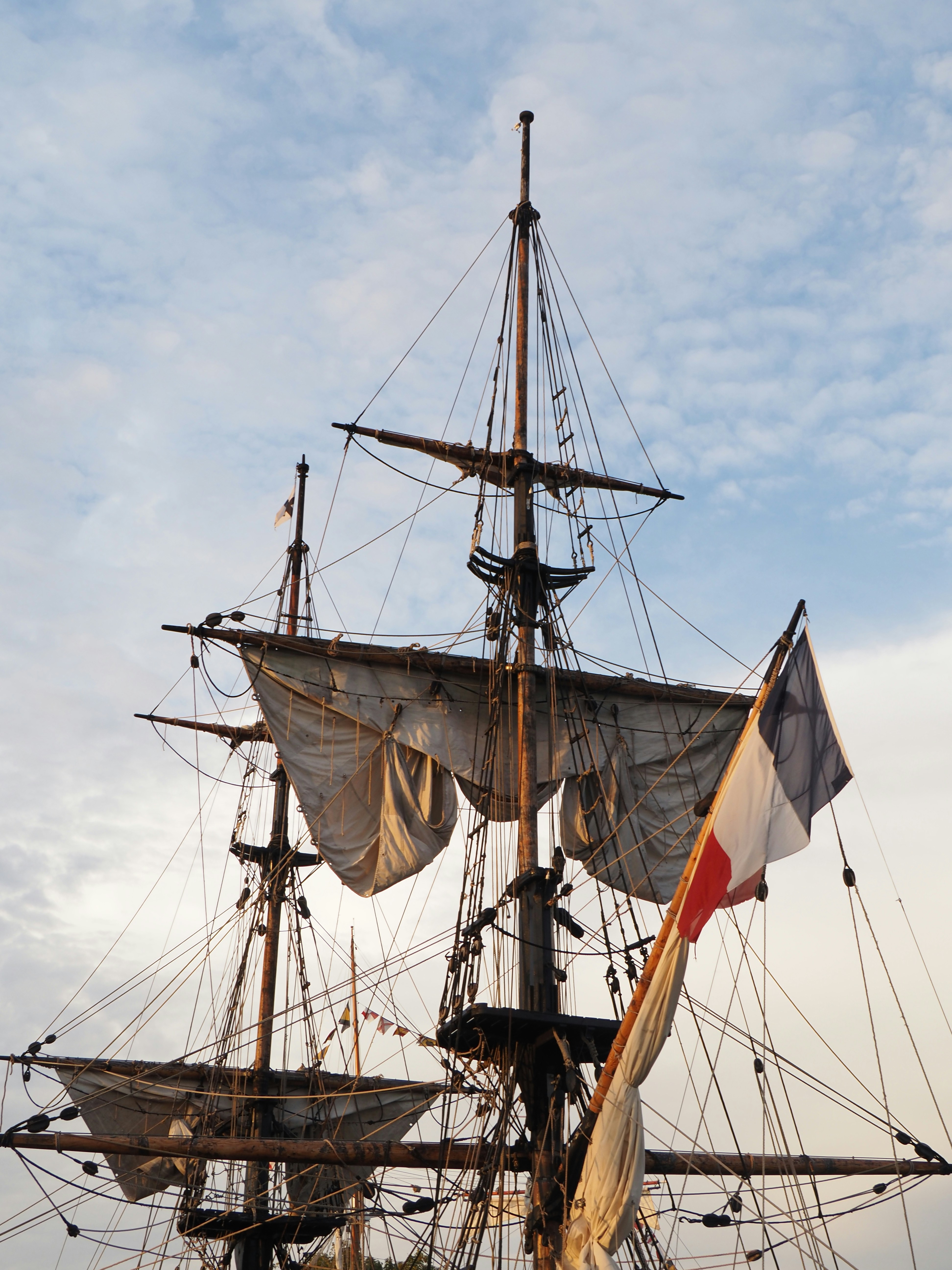 Masts and furled sails of a tall ship with a French flag flying