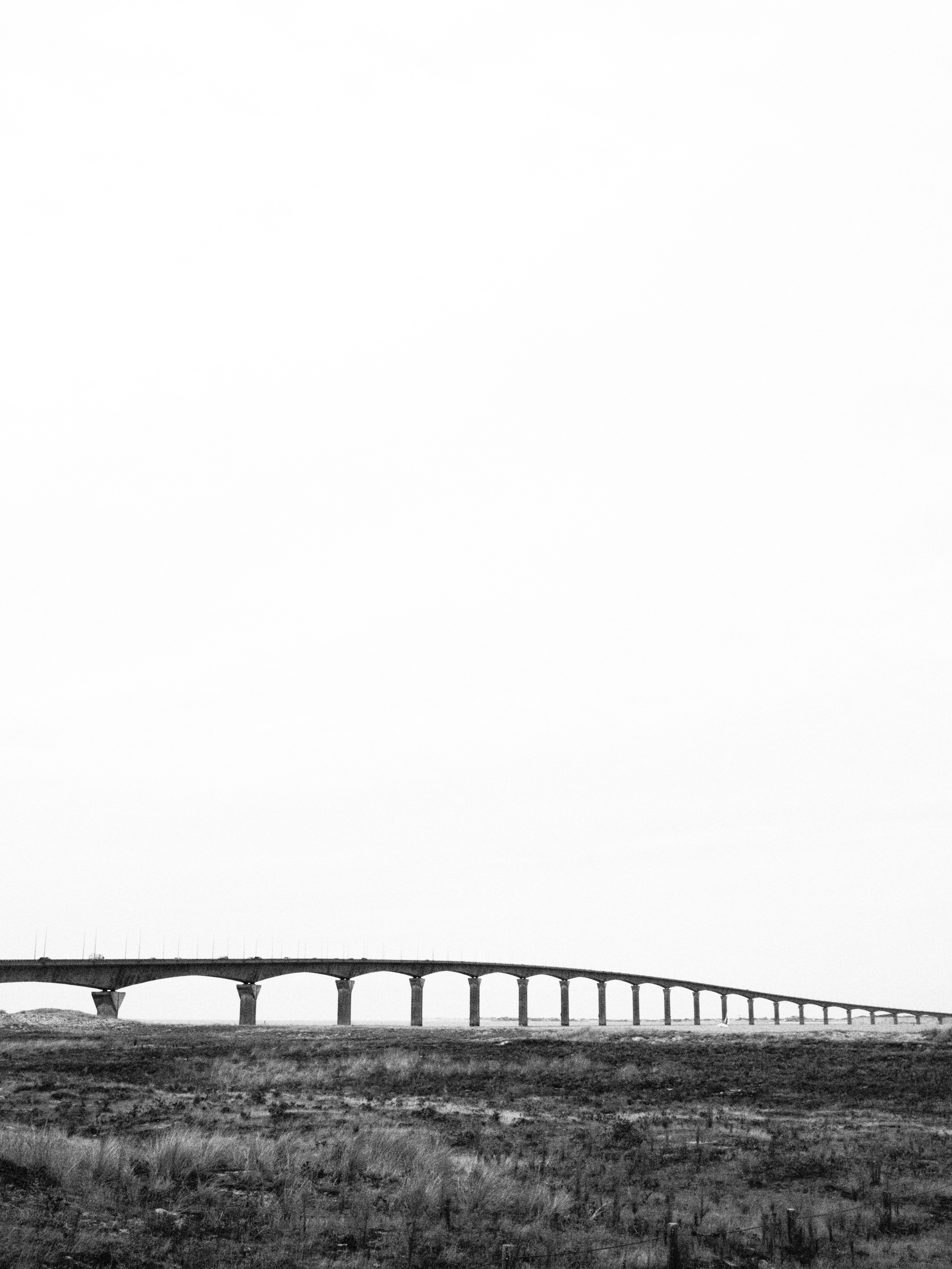 A long concrete bridge spanning across a flat grassy landscape under a bright sky