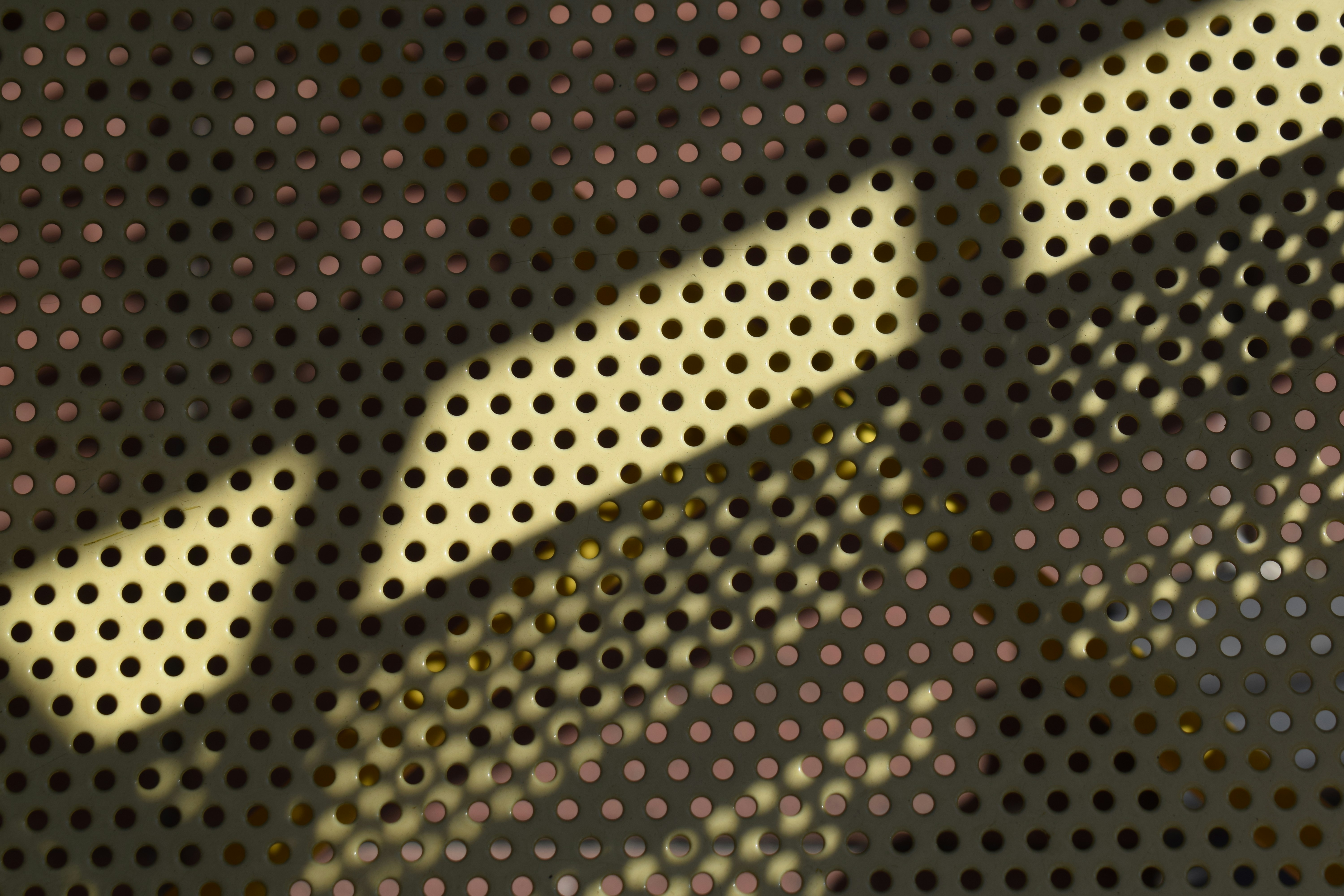 A perforated metal sheet with diagonal shadows cast across the circular holes