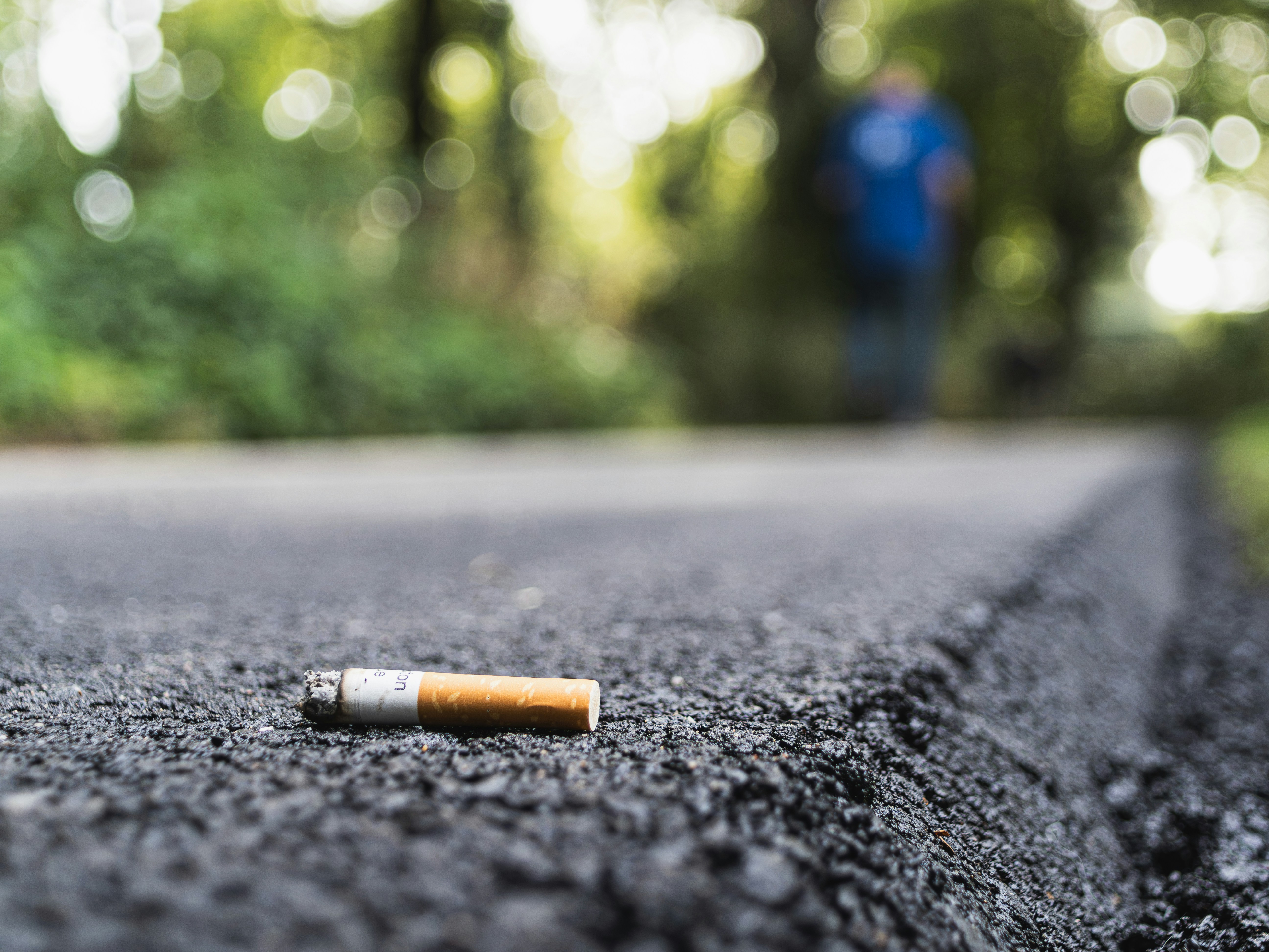 Un mégot de cigarette abandonné sur une route asphaltée sombre avec une personne floue marchant