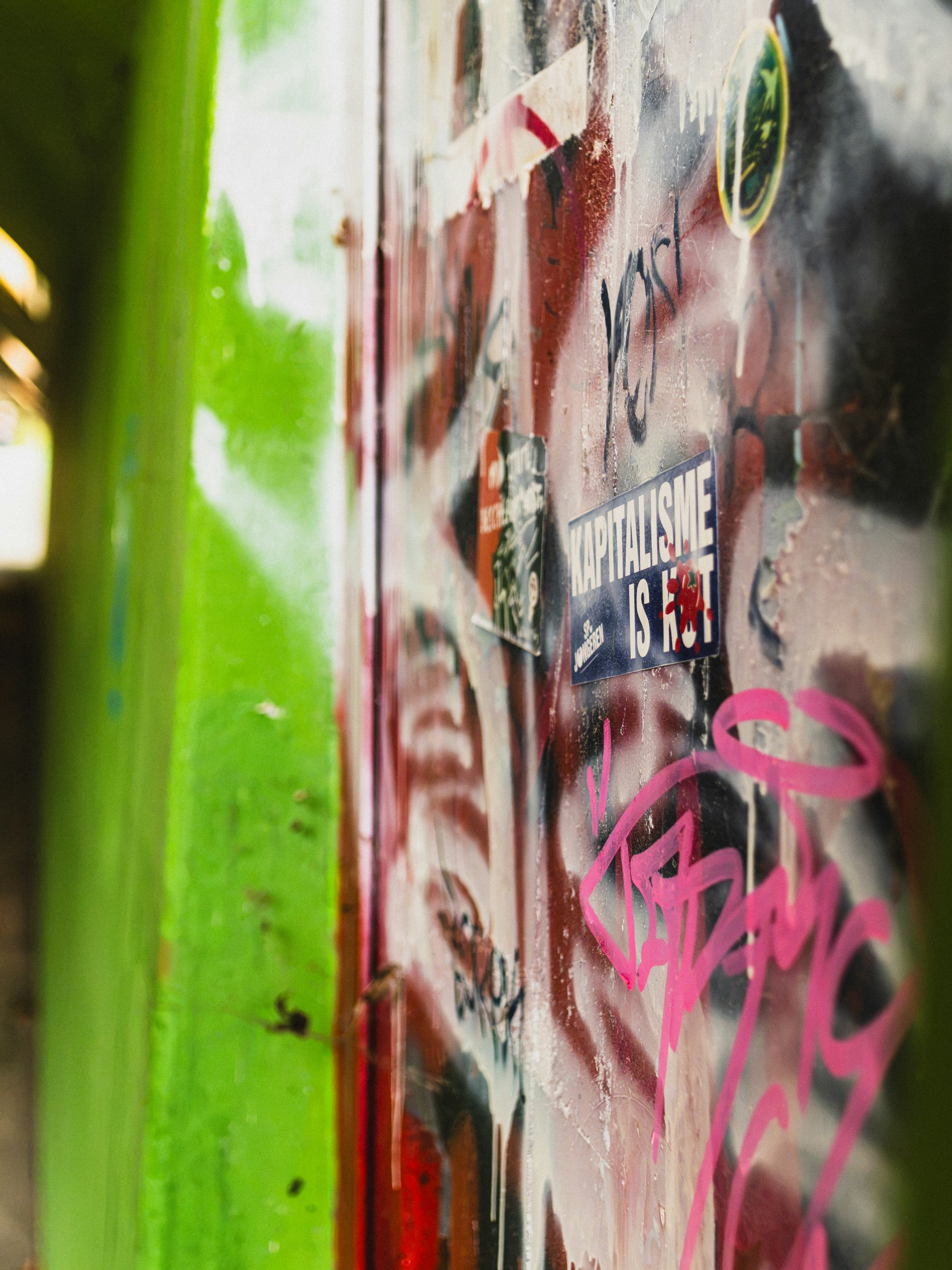 Un mur vert vif à côté d’une surface couverte de graffitis superposés et d’autocollants