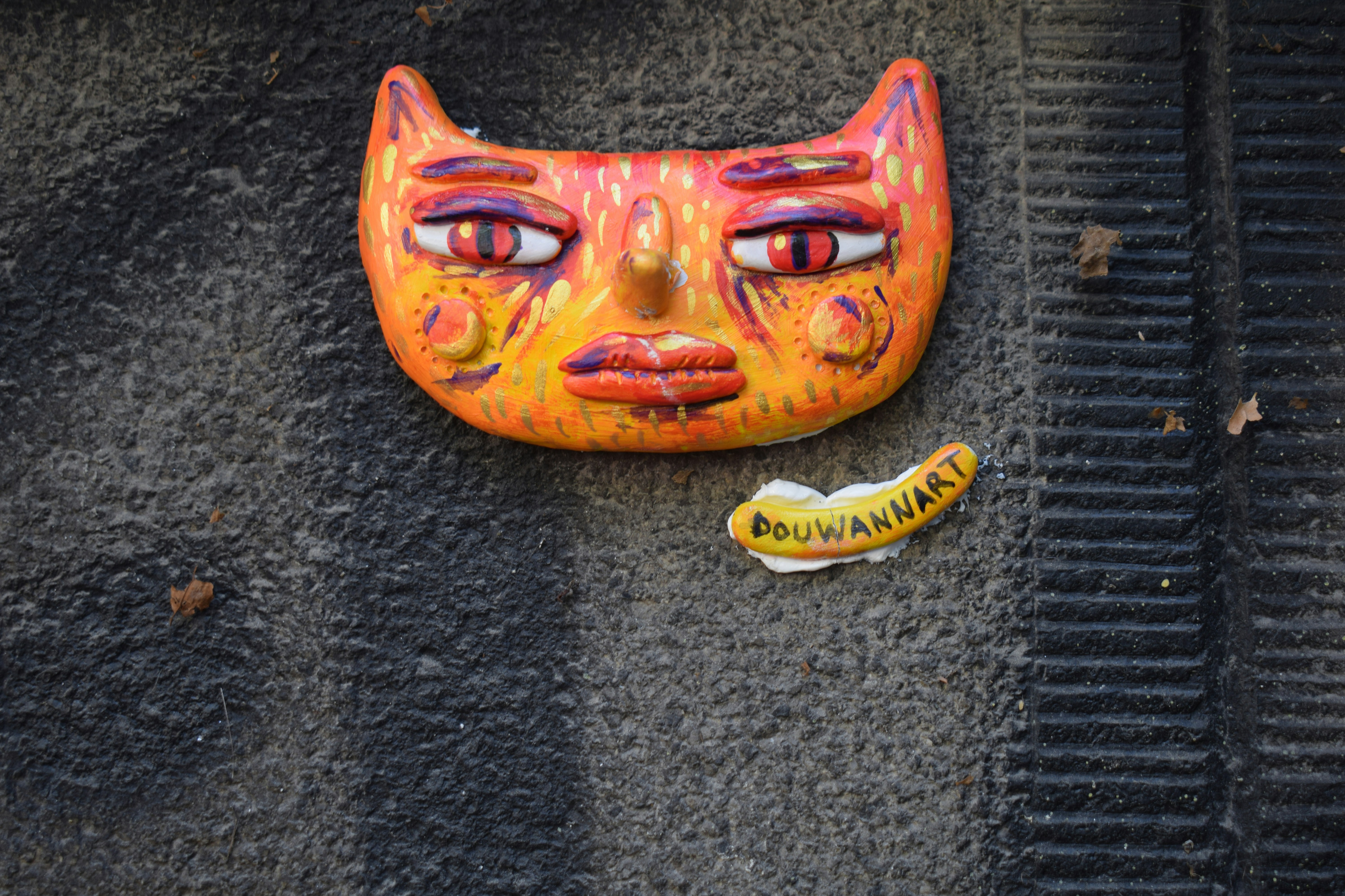 A colorful ceramic cat face mask mounted on a dark textured wall