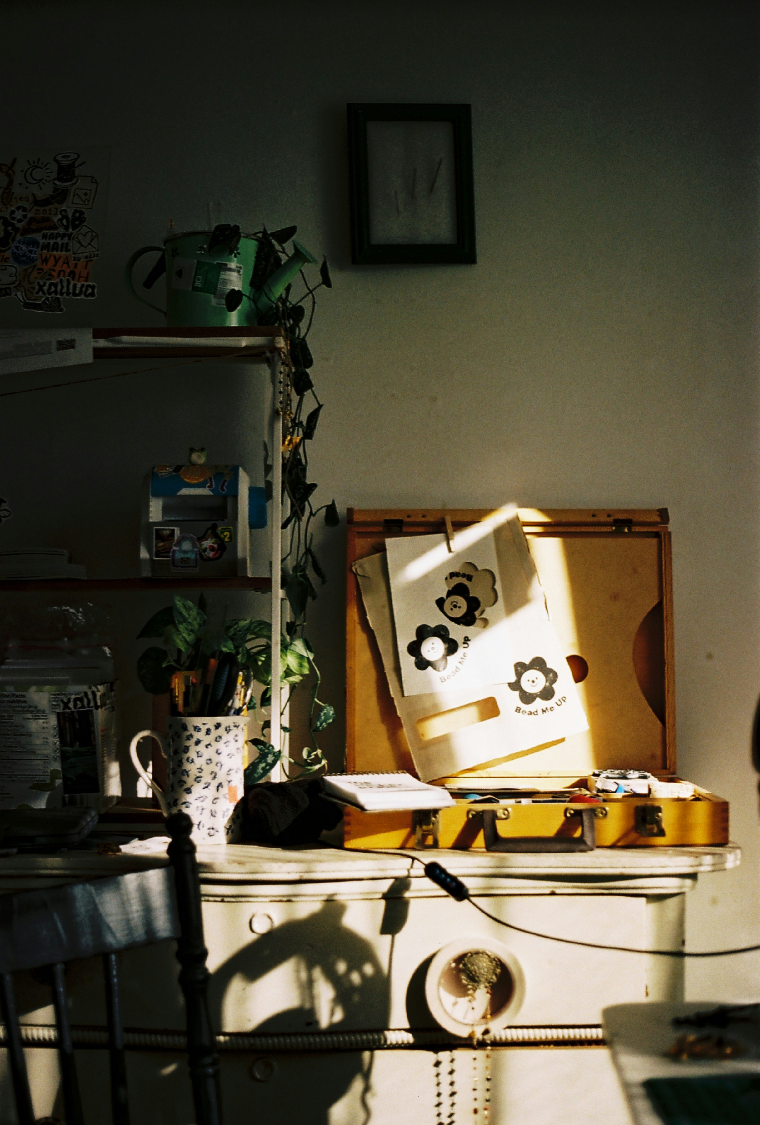 A sunlit wooden art case and a mug with pens on a white desk
