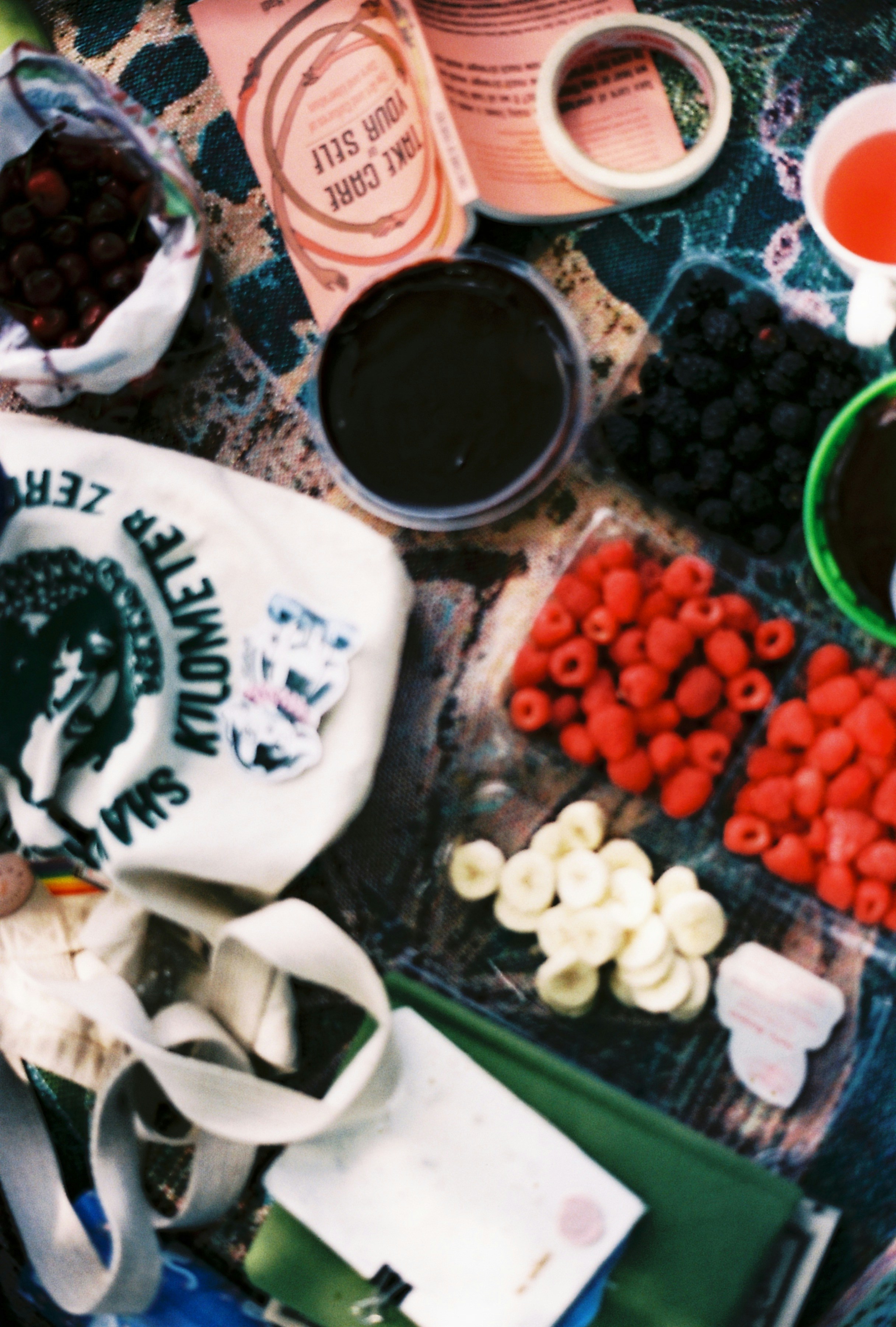A picnic spread with raspberries, blackberries, sliced bananas, cherries, and chocolate on a patterned blanket