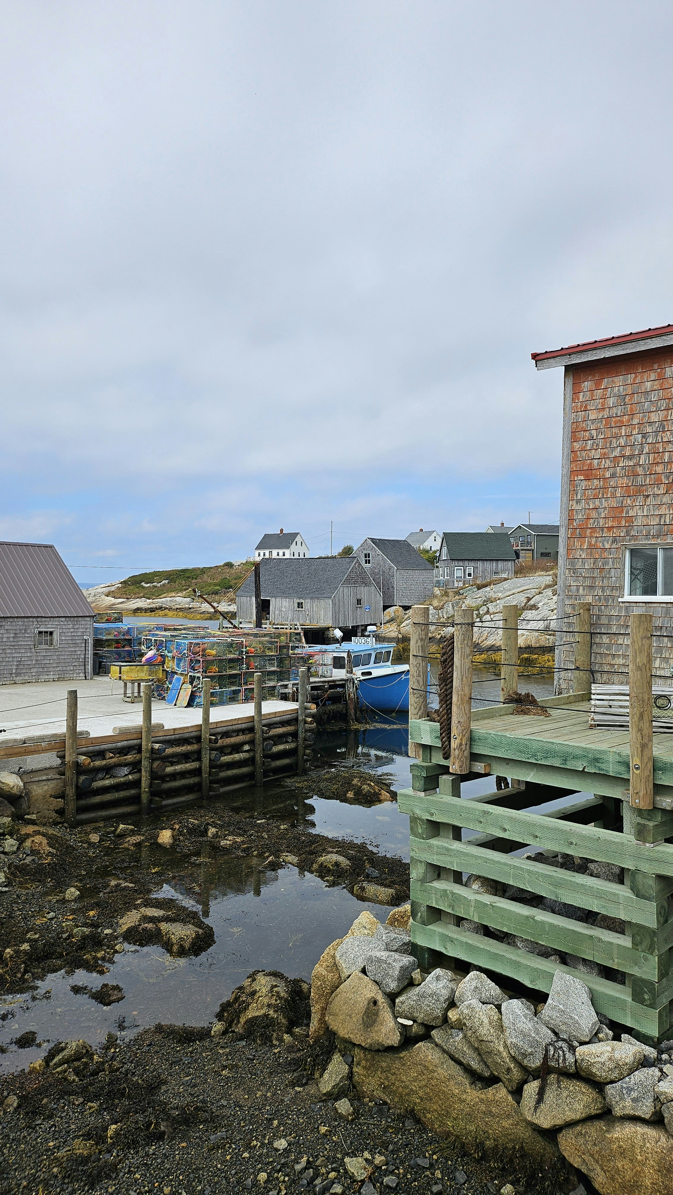 A blue boat moored at a wooden dock with stacked lobster traps nearby