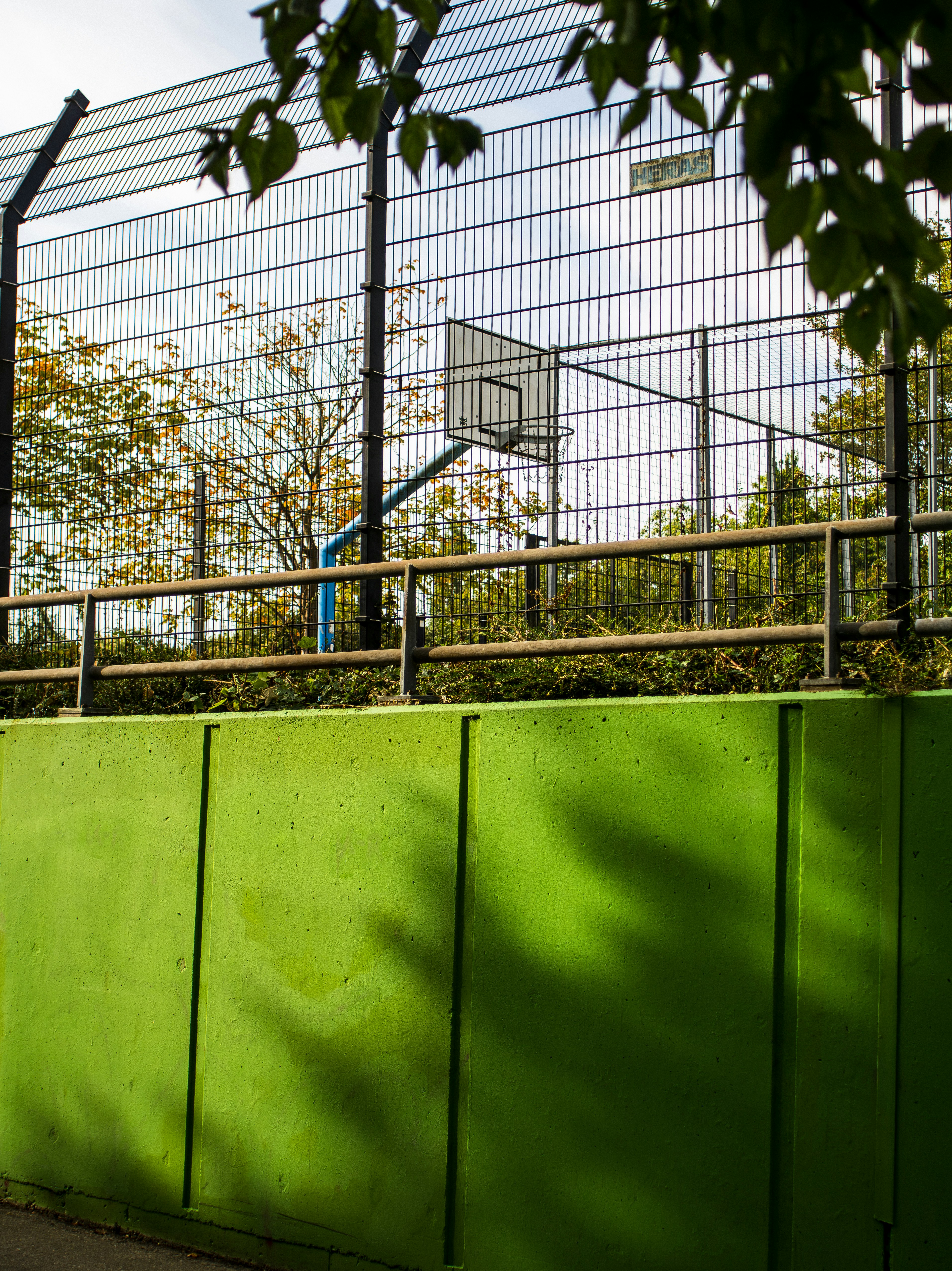 Un panier de basket derrière une haute clôture en fil de fer au-dessus d’un mur vert vif
