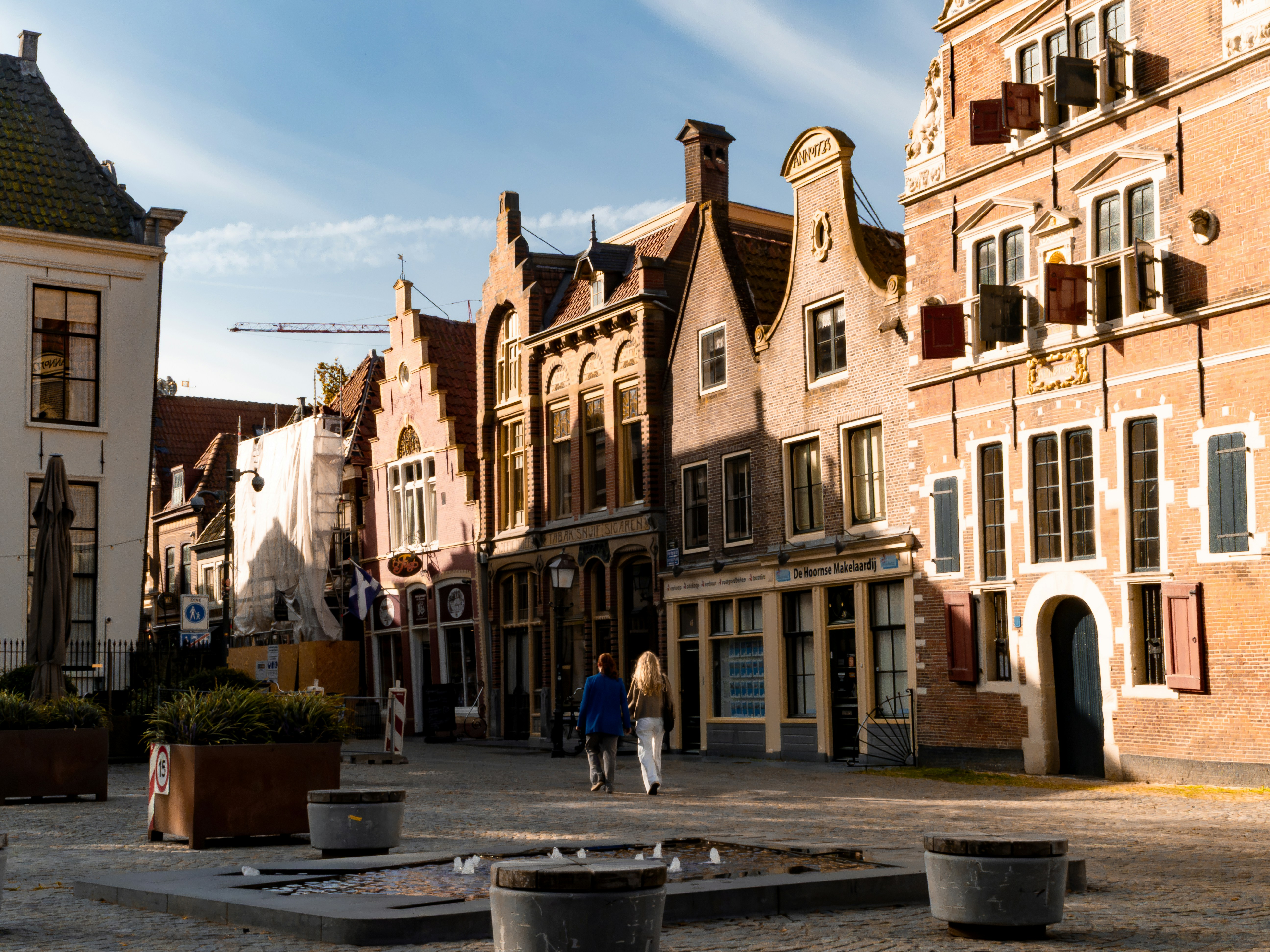 Two people walking on a cobblestone square past historic brick buildings in Hoorn