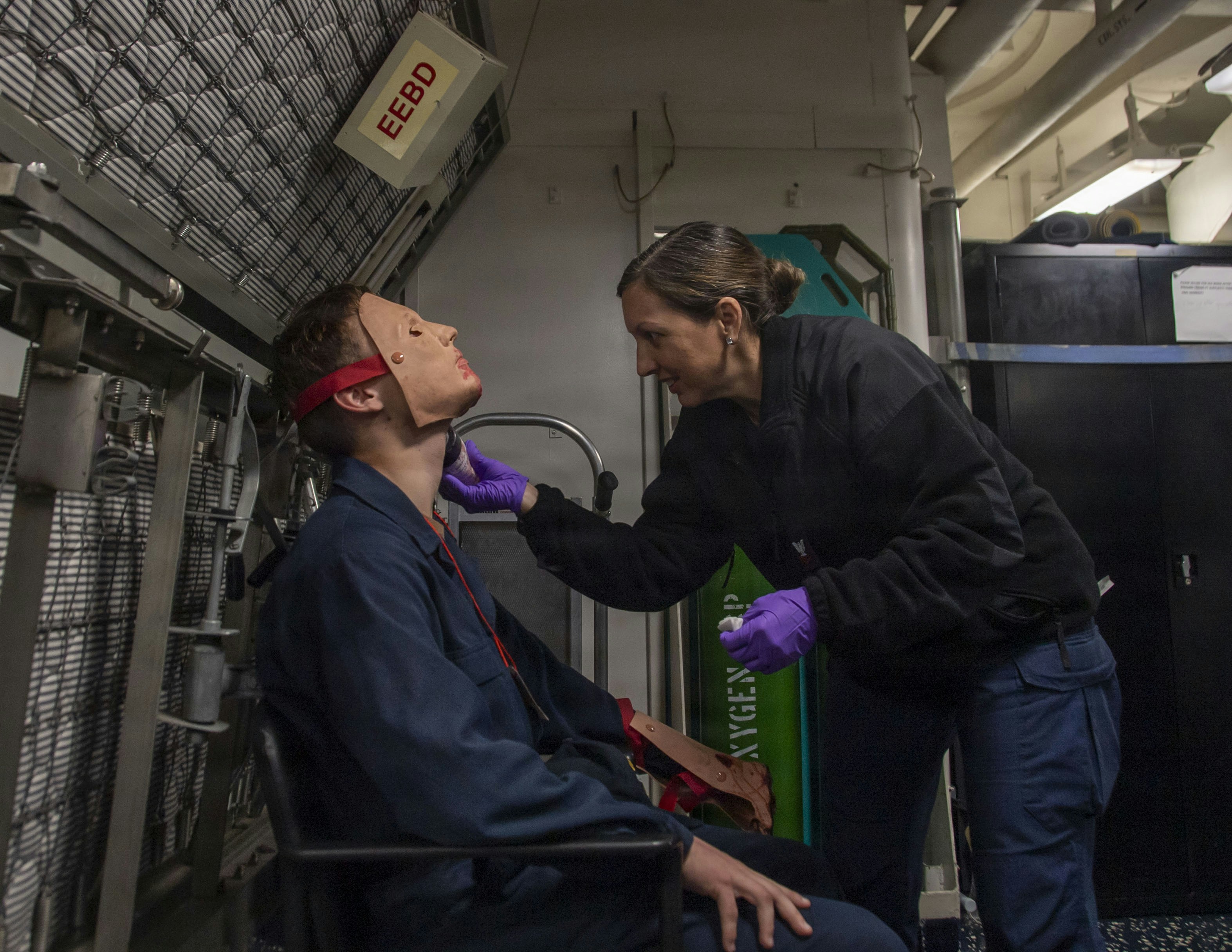 A woman in a black fleece applying makeup to a person wearing a prosthetic mask