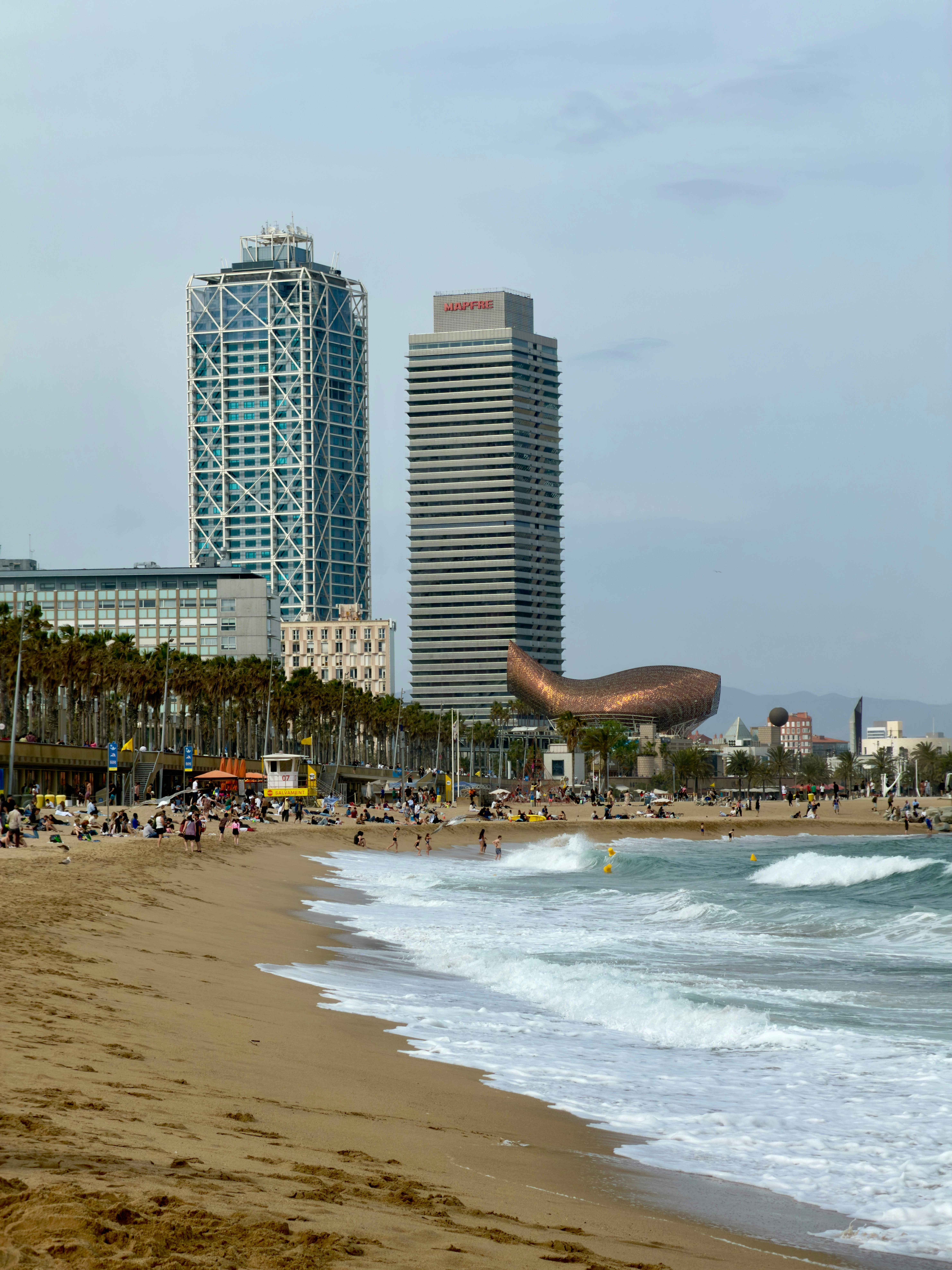 People on Barceloneta Beach with the Frank Gehry Fish sculpture and skyscrapers in Barcelona